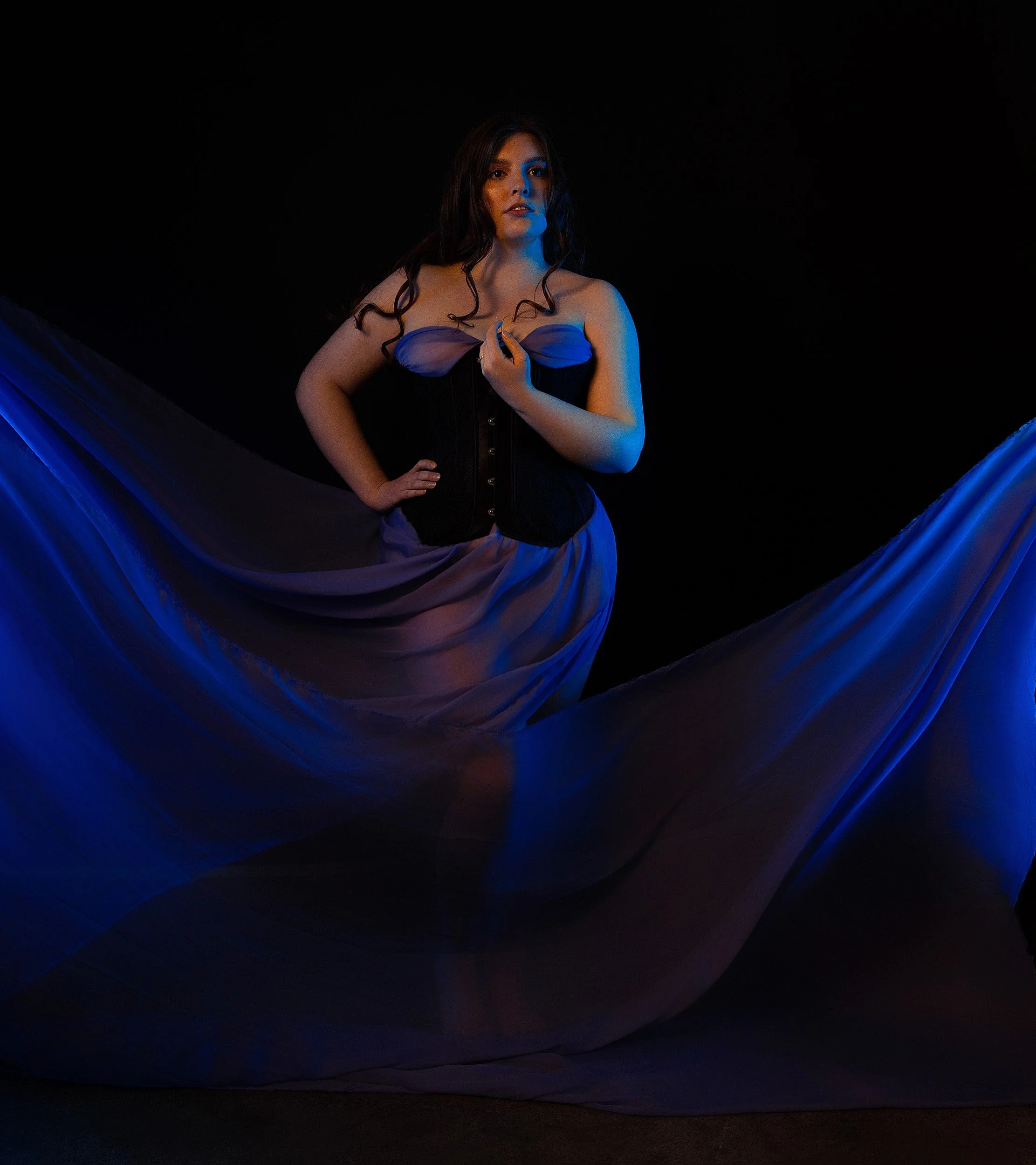 Luxury boudoir portrait of a woman in black lingerie framed by sweeping blue fabric with dramatic editorial lighting in Vancouver, WA.