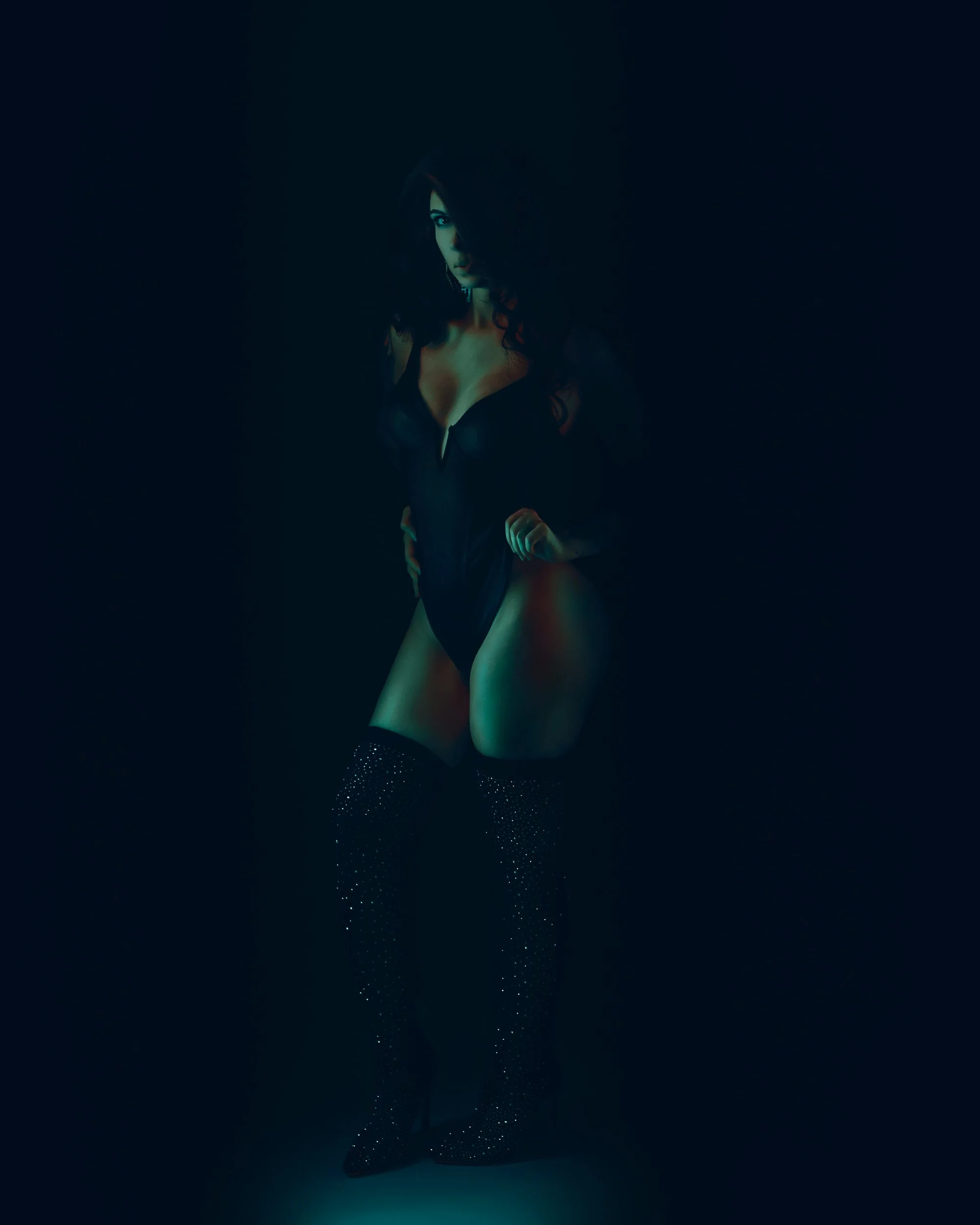 Editorial boudoir portrait by Amanda Chantee featuring a woman in black lingerie and thigh-high boots under cinematic teal studio lighting.