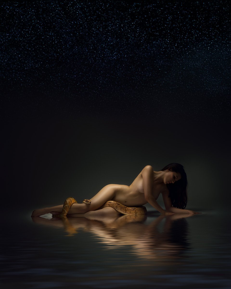 Fine art nude portrait in Vancouver, WA, featuring a woman reclining on a reflective floor beneath soft falling water and low-key studio light.
