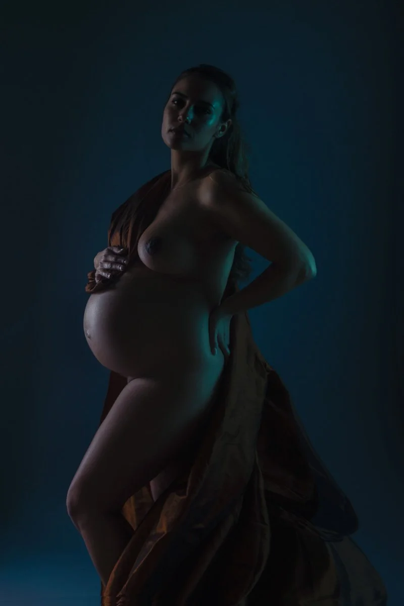 Fine art maternity portrait by Amanda Chantee in Vancouver, WA, featuring a pregnant woman posed under dramatic teal and warm studio lighting.
