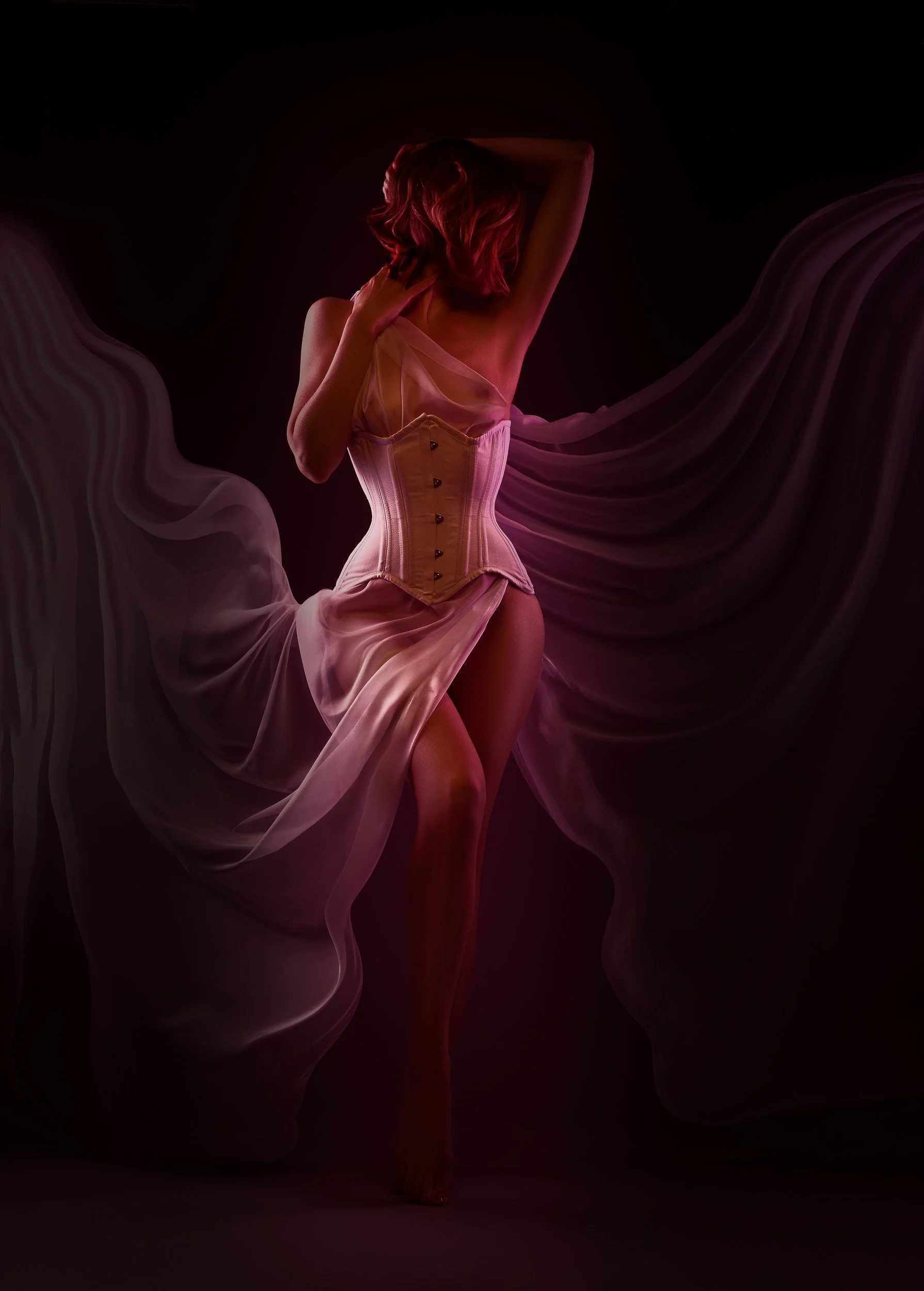 Fine art boudoir portrait in Vancouver, WA, featuring a woman in a corset framed by flowing fabric under rich red and purple studio lighting.