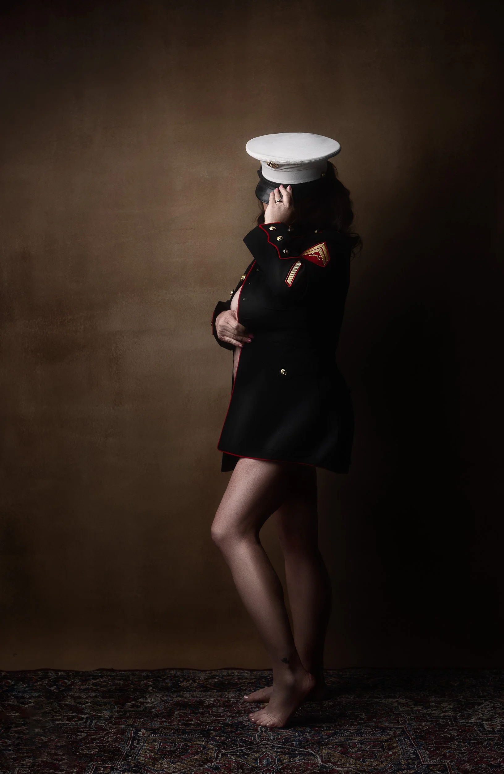 Editorial boudoir portrait of a woman in a military-style jacket and hat photographed against a warm neutral backdrop near Portland, Oregon.