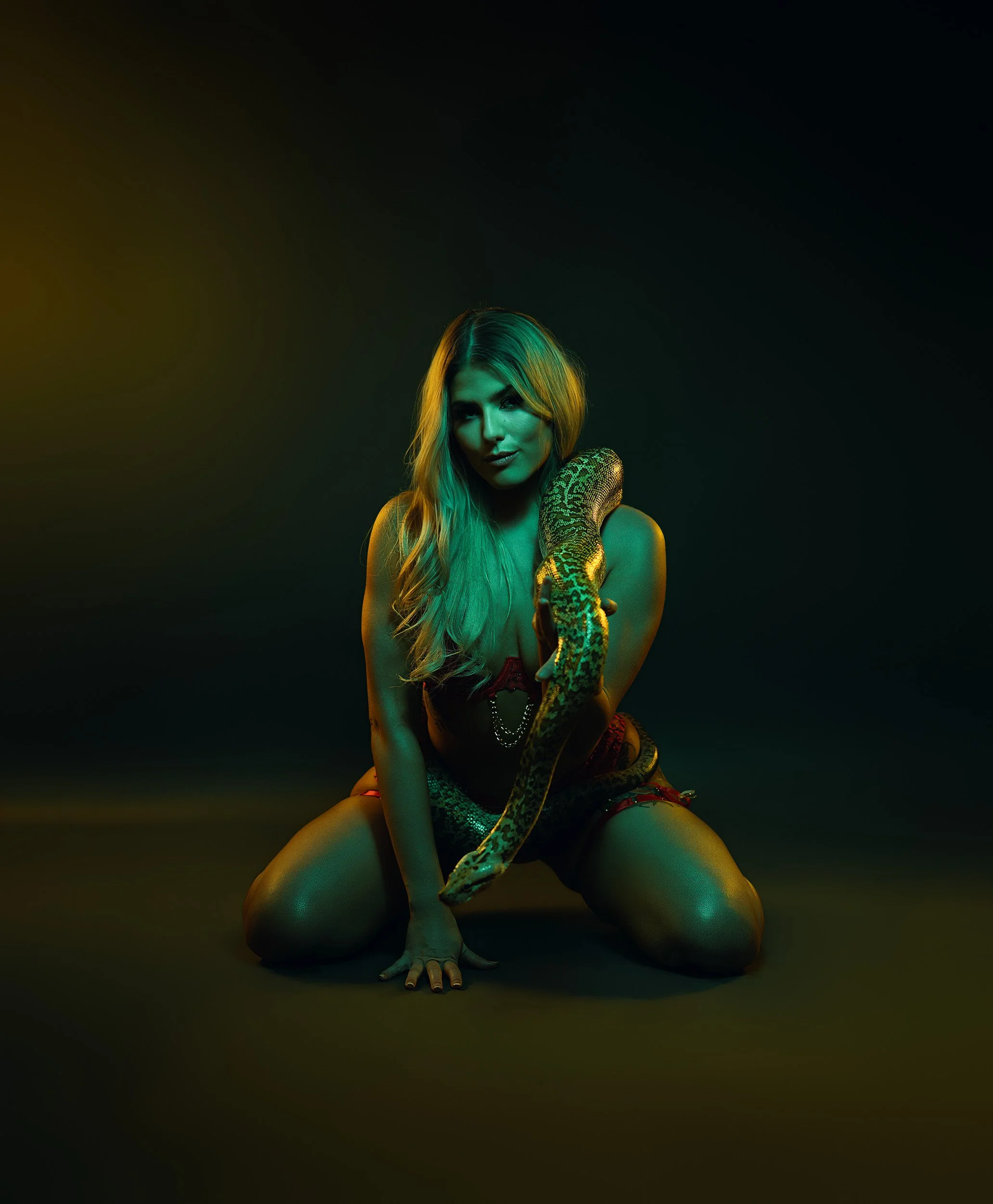 Woman kneeling in black lingerie under dramatic green and gold studio lighting during a fine art boudoir session.