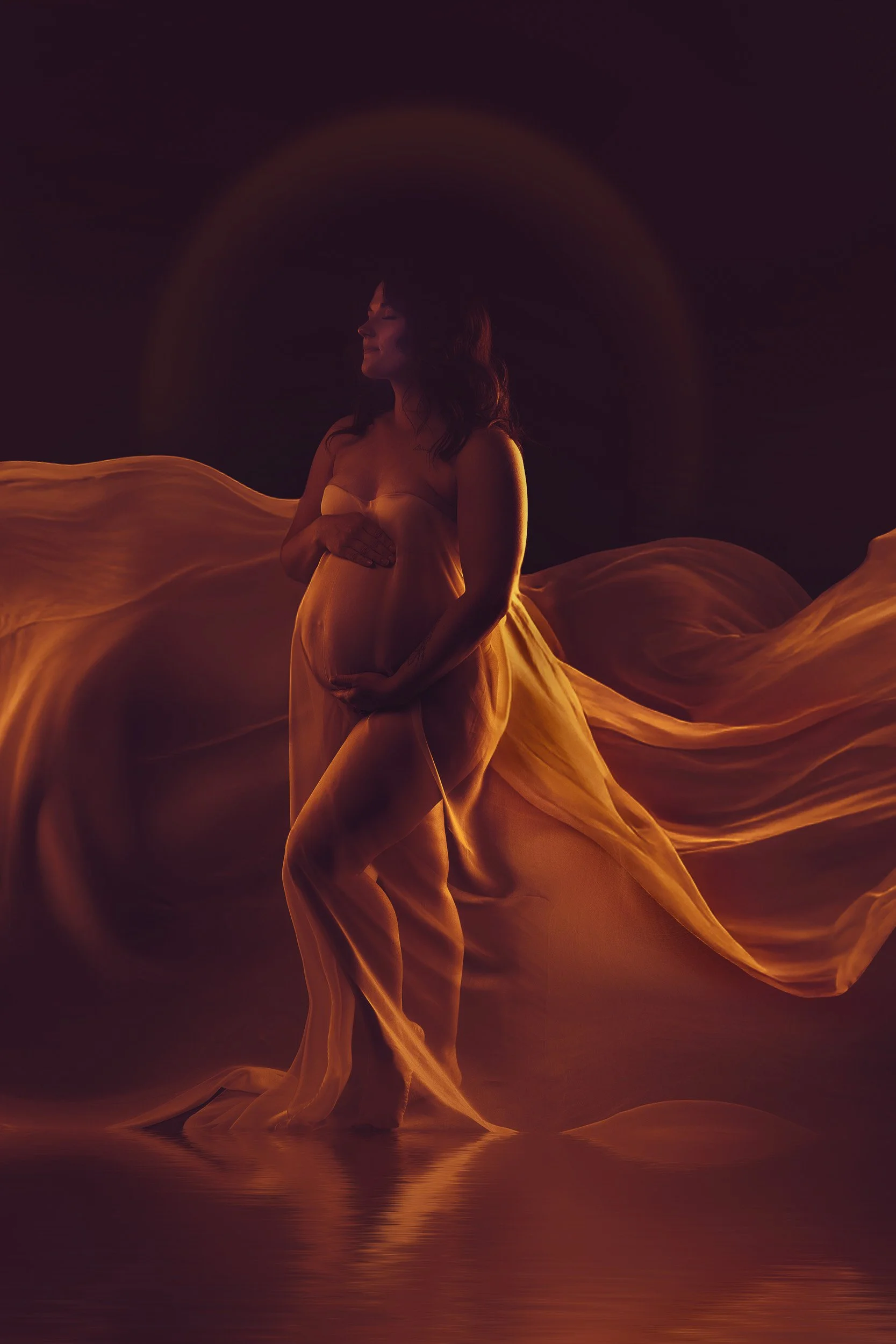 Vancouver WA maternity portrait featuring a pregnant woman surrounded by flowing golden fabric under rich amber and purple studio lighting.