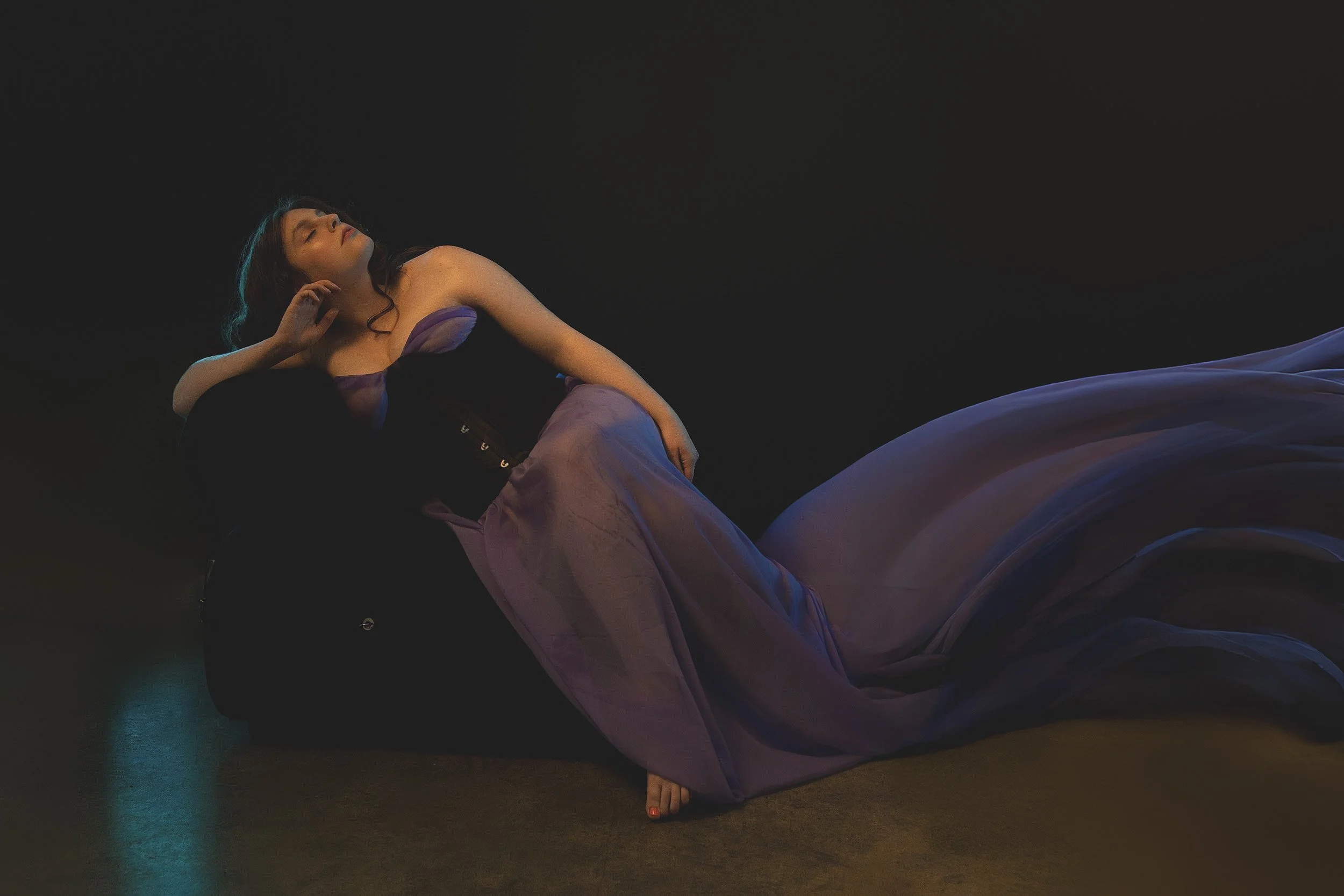 Artistic boudoir portrait by Amanda Chantee of a woman reclining in black lingerie with flowing blue fabric and moody studio light.