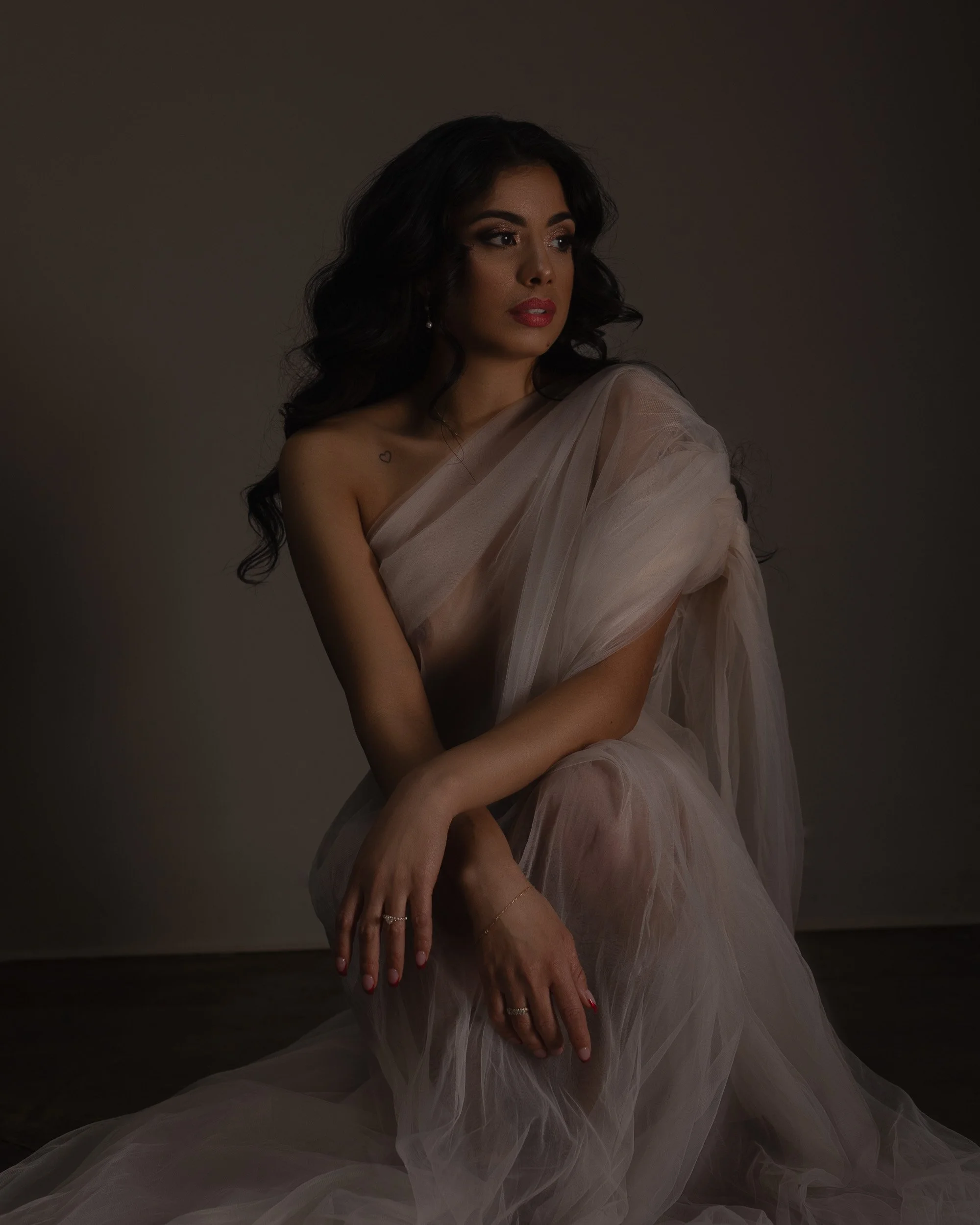 Luxury boudoir portrait near Portland, Oregon, featuring a woman seated in sheer white draping under soft editorial light.