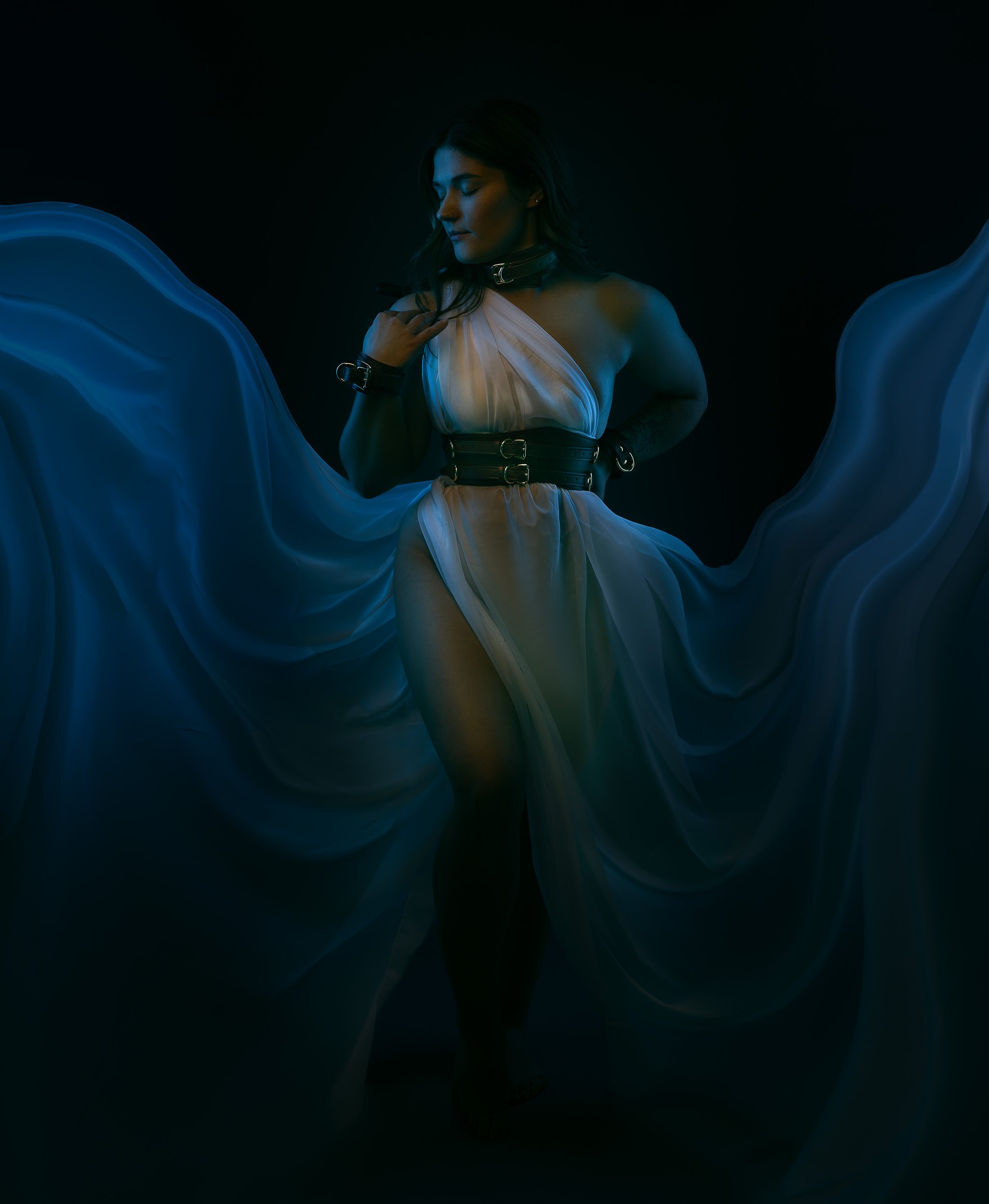 Luxury boudoir photography by Amanda Chantee featuring a woman in lingerie framed by flowing blue fabric and dramatic studio light.