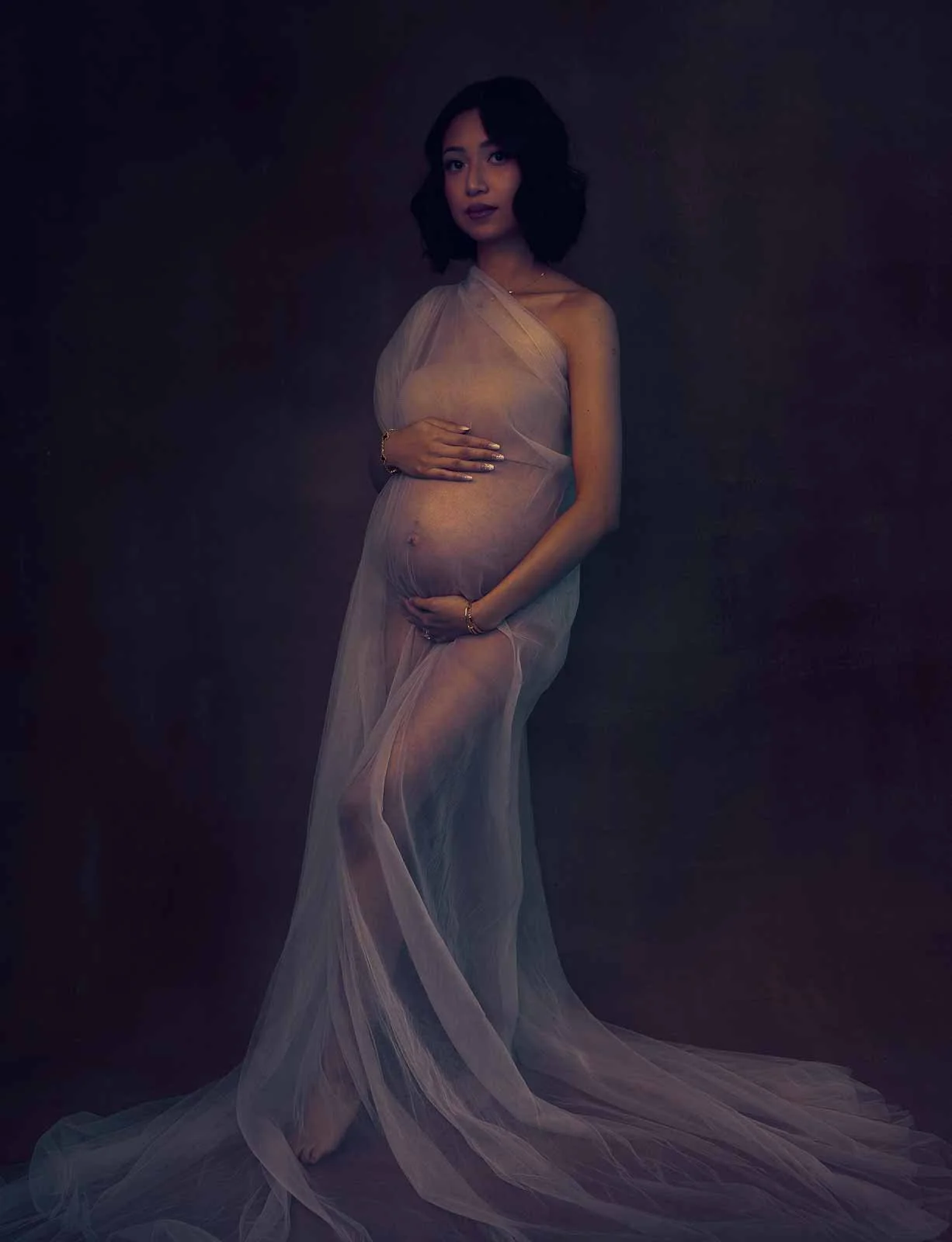 Fine art maternity photography by Amanda Chantee featuring a pregnant woman in flowing sheer lavender fabric under soft moody studio lighting.