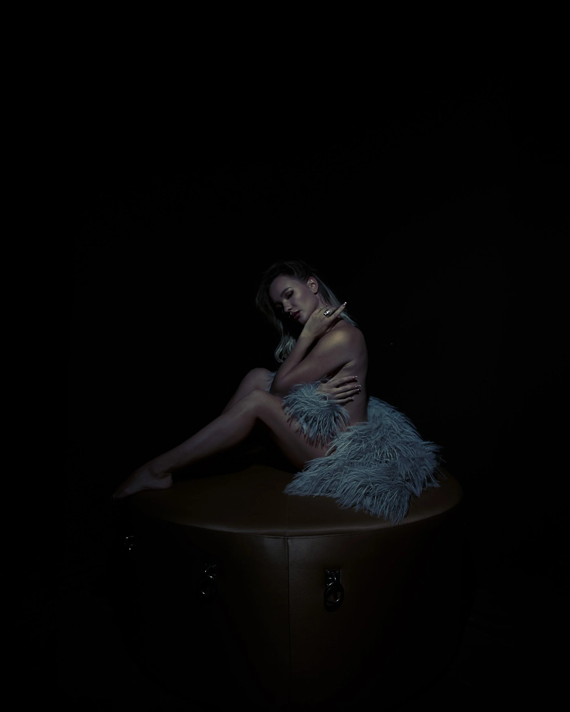 Las Vegas boudoir portrait of a woman wrapped in golden faux fur, seated on a round bench with dramatic blue and gold studio lighting by Amanda Chantee