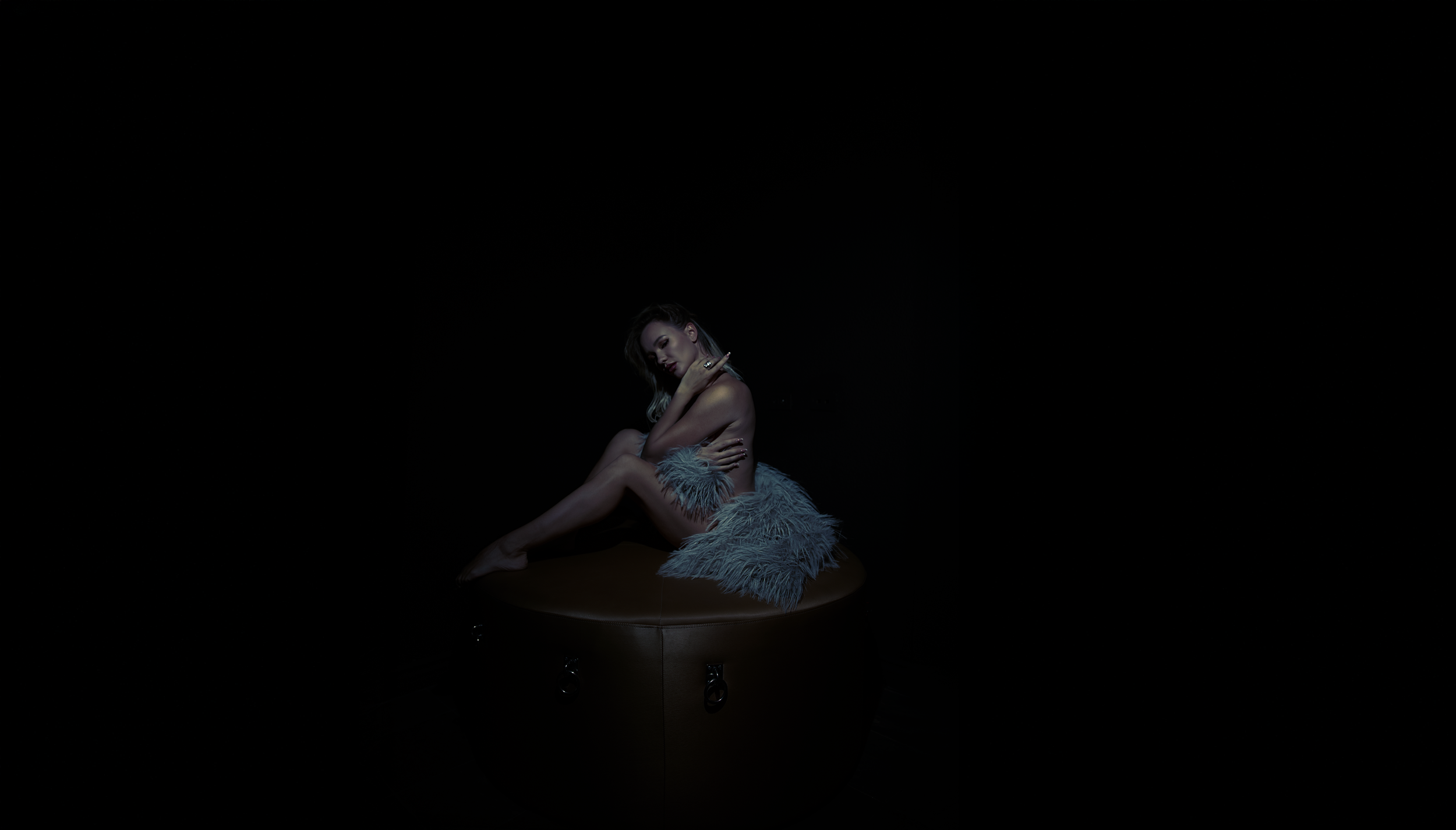 Las Vegas boudoir portrait of a woman wrapped in golden faux fur, seated on a round bench with dramatic blue and gold studio lighting by Amanda Chantee