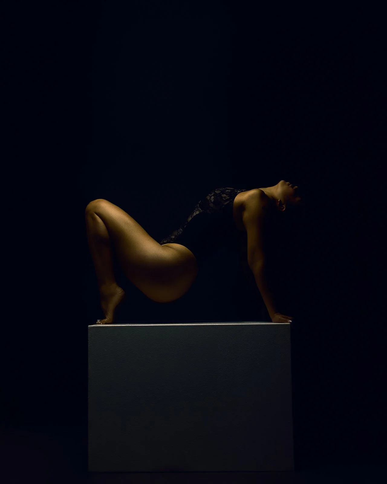 Fine art boudoir portrait by Amanda Chantee in Vancouver, WA, featuring a woman reclining on a pedestal under dramatic blue and amber lighting.
