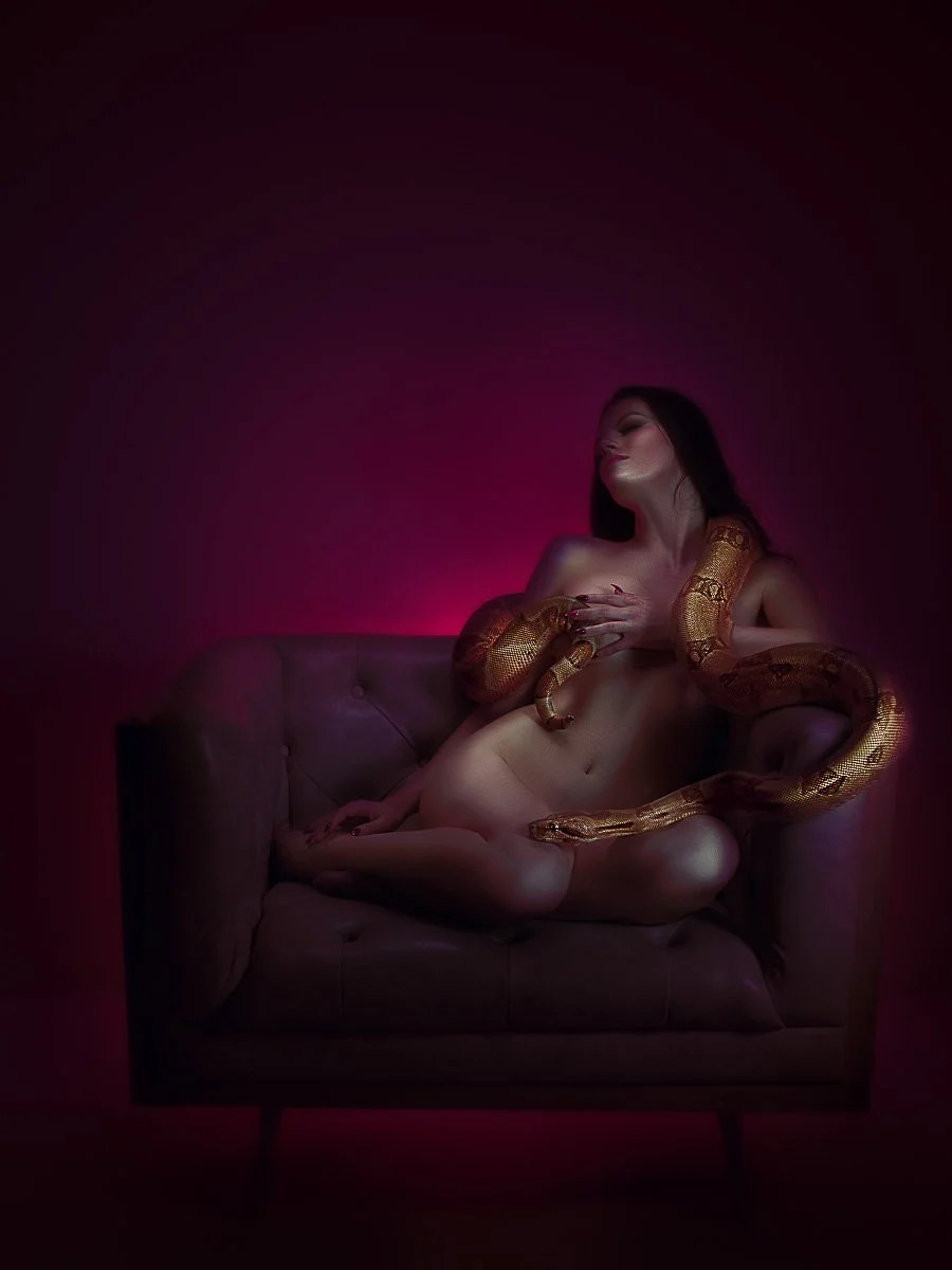 Moody artistic boudoir portrait by Amanda Chantee of a woman seated on a sofa beneath magenta lighting with soft motion blur.