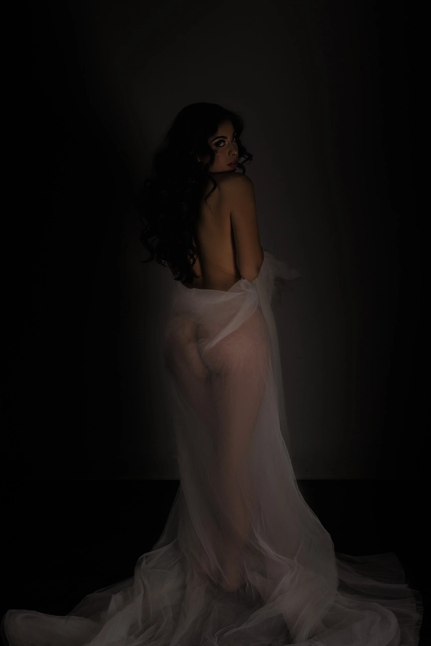 Fine art boudoir portrait in Vancouver, WA, featuring a woman wrapped in sheer white fabric under soft dramatic studio lighting.