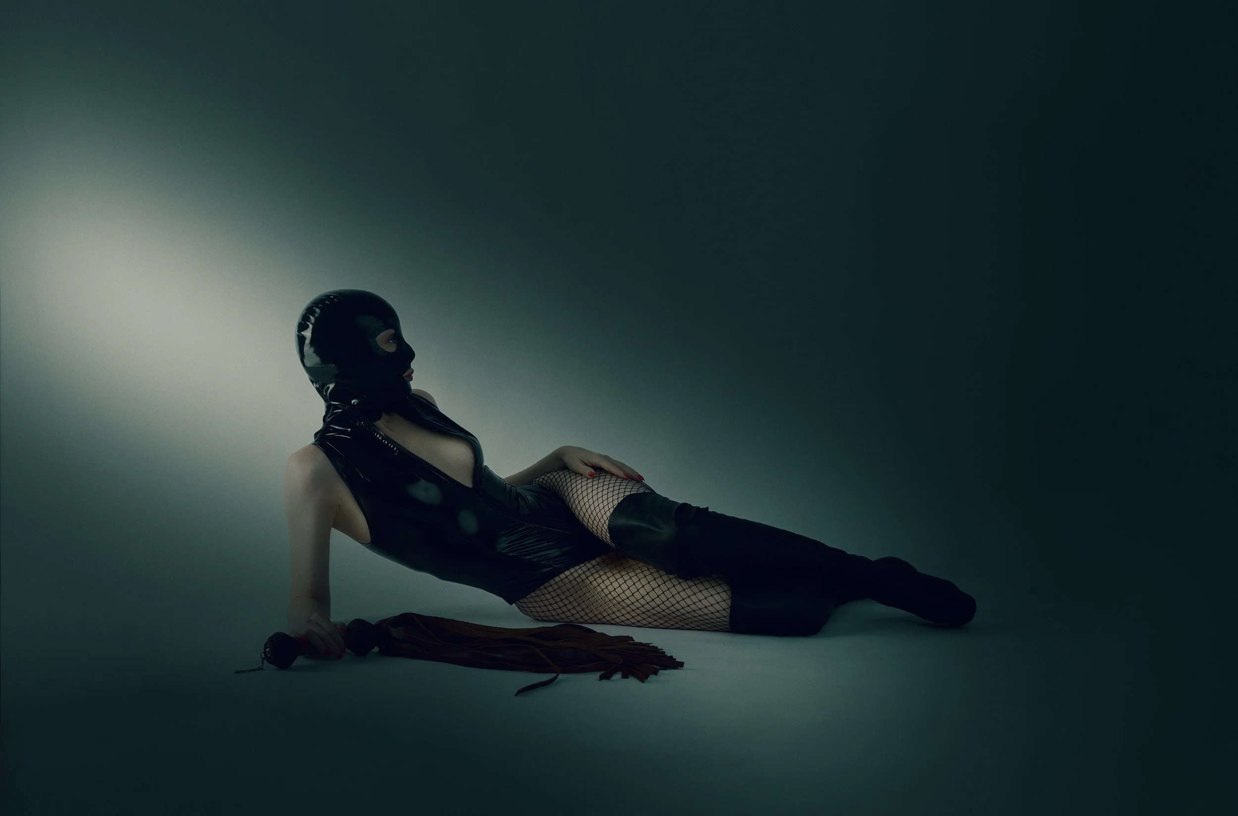 Artistic fine art boudoir portrait of a woman reclining on the floor in black lingerie under cool teal studio lighting.