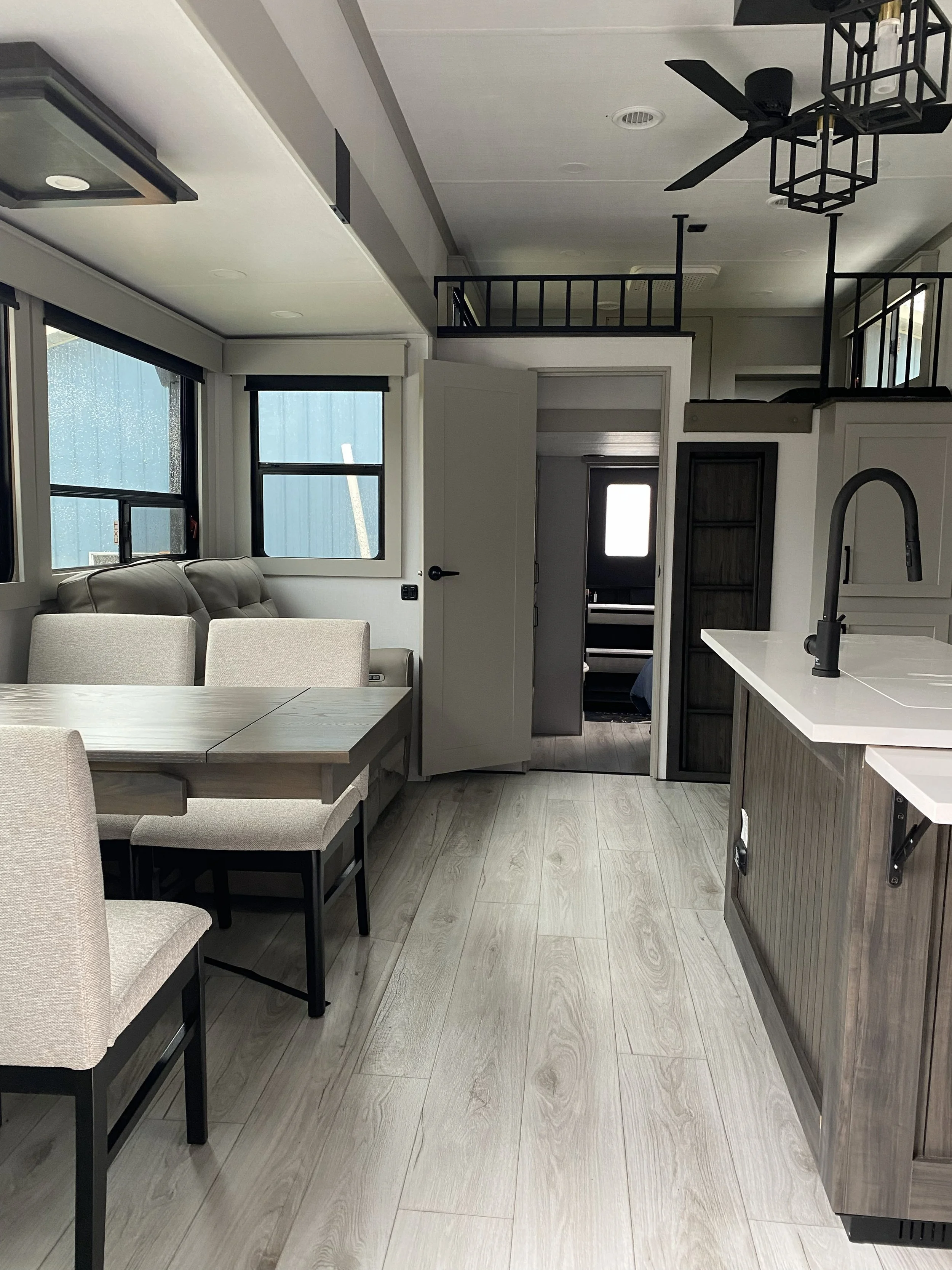 Interior of a modern home with a dining area, kitchen island with a sink, a couch, windows, and a second floor with a balcony.