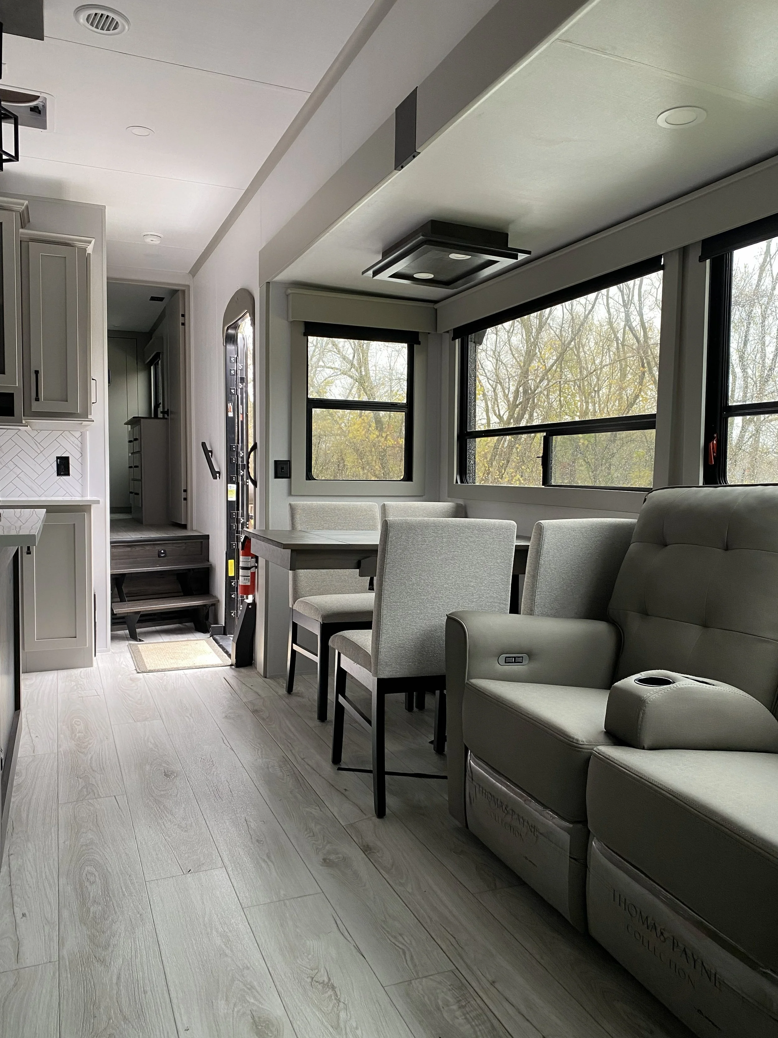Interior of a modern living space with large windows, a dining table with chairs, and a reclining chair.