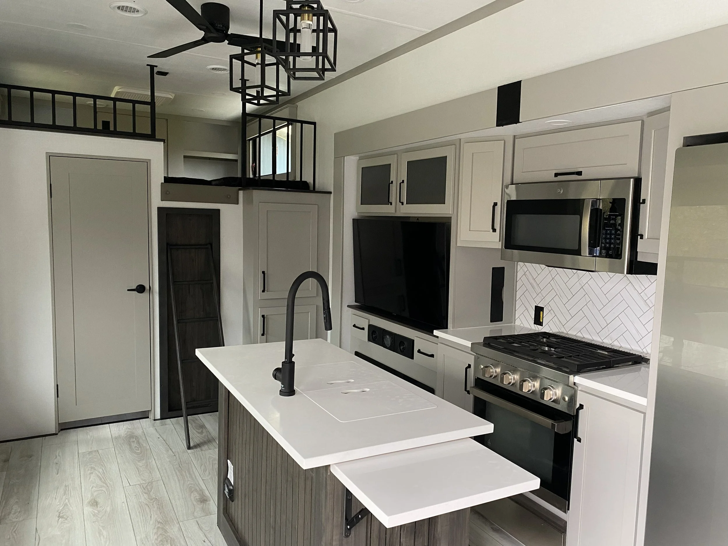 Modern kitchen with white cabinets, stainless steel appliances, a black faucet, and a white kitchen island with a fold-out tray.