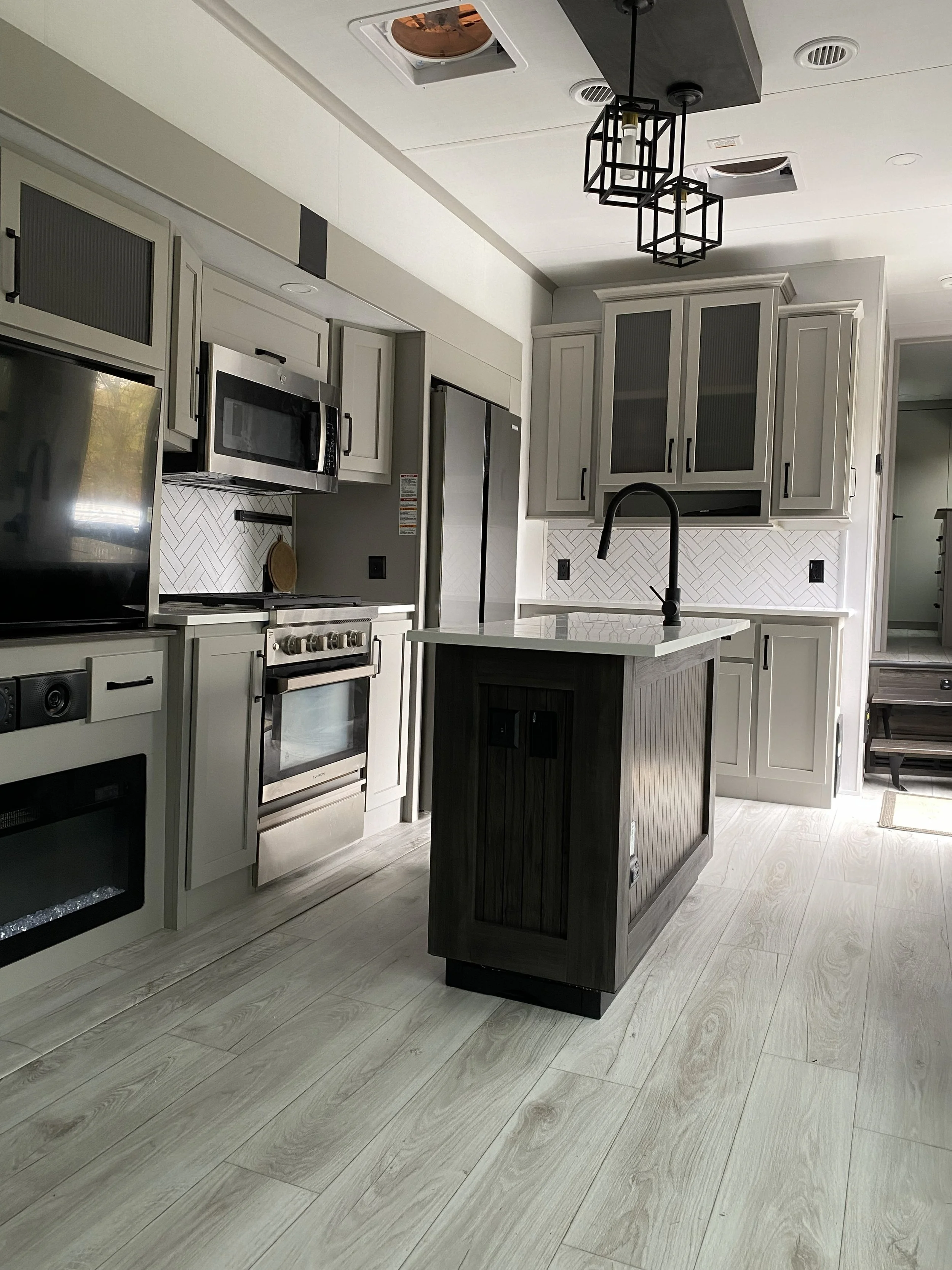 Modern kitchen with light gray cabinets, white backsplash, stainless steel appliances, and a dark kitchen island with a white countertop.