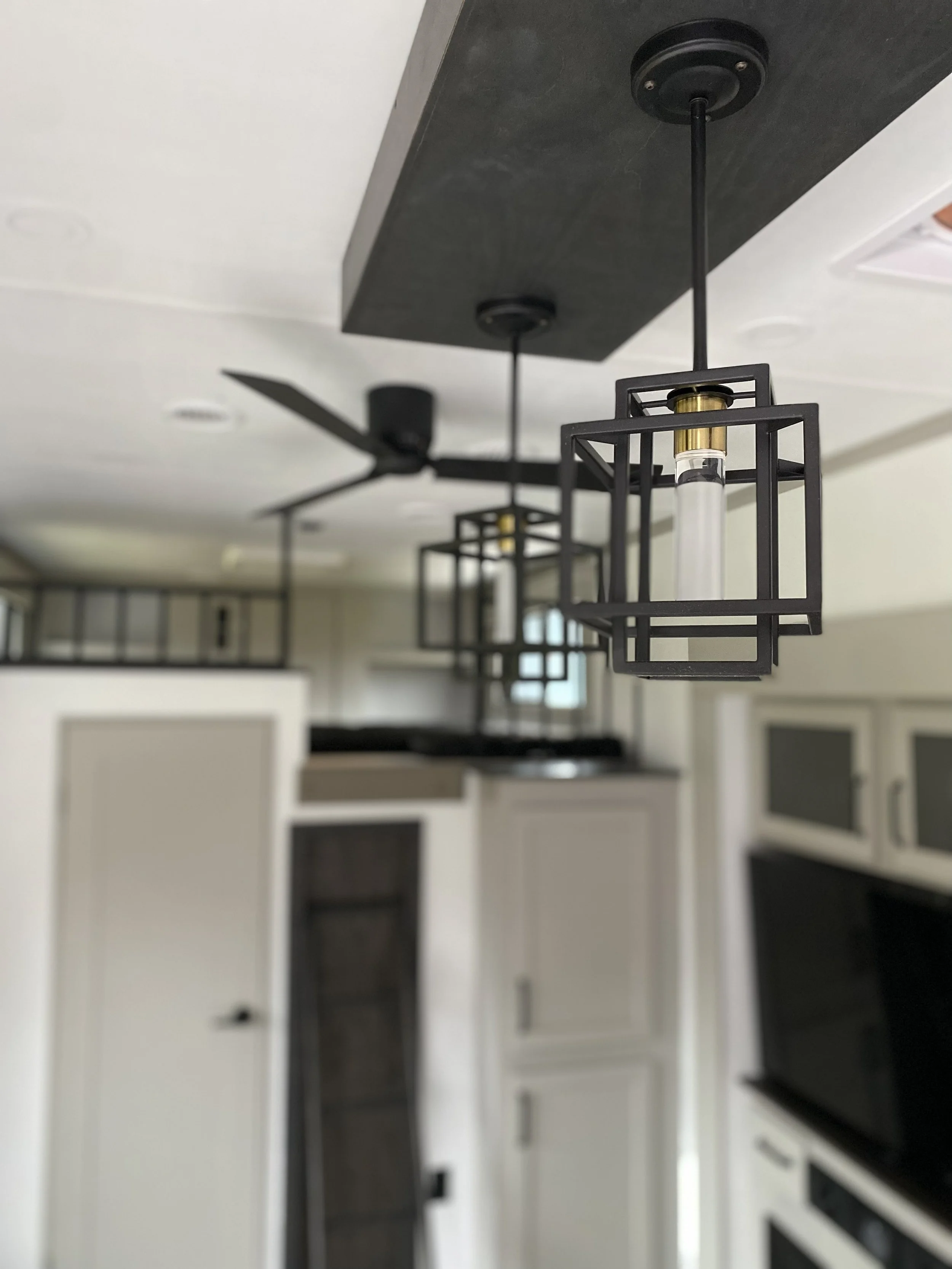 Close-up of two modern black metal pendant light fixtures hanging from ceiling with black ceiling mount in a kitchen with white cabinets and black accents.