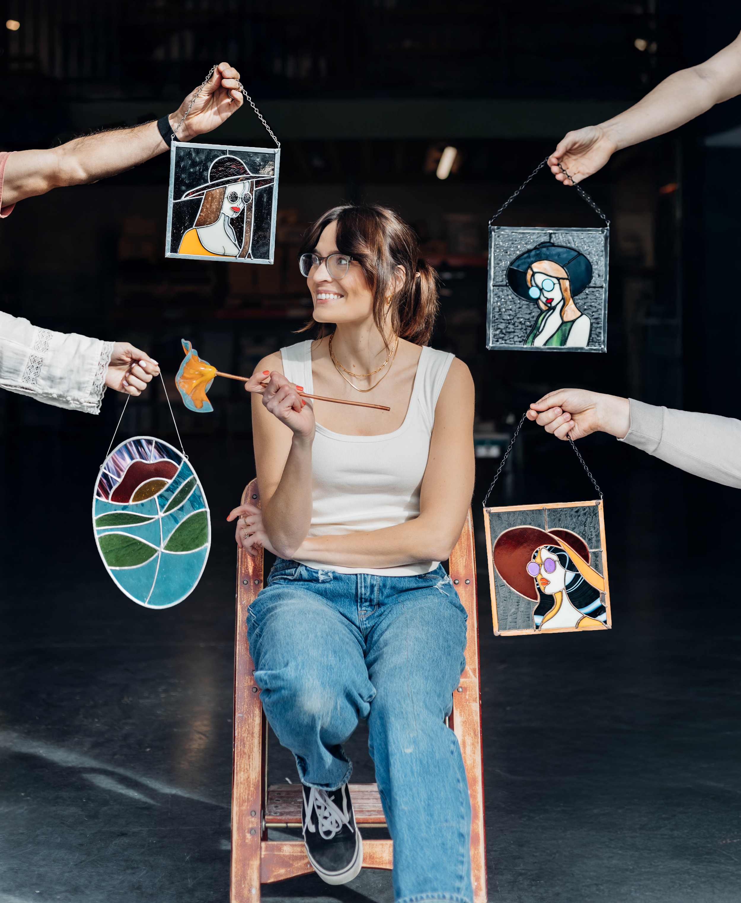 Smiling woman seated on a ladder surrounded by her stained glass artwork