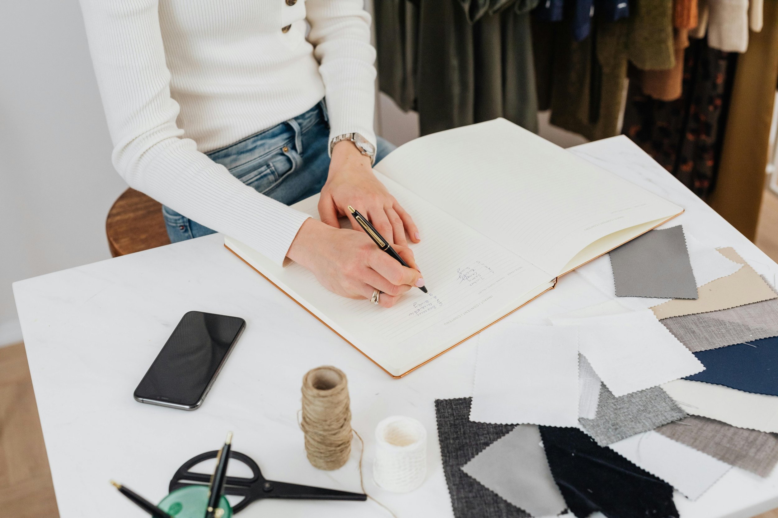 Person writing in a large open notebook on a white table, planning content and growth strategies.