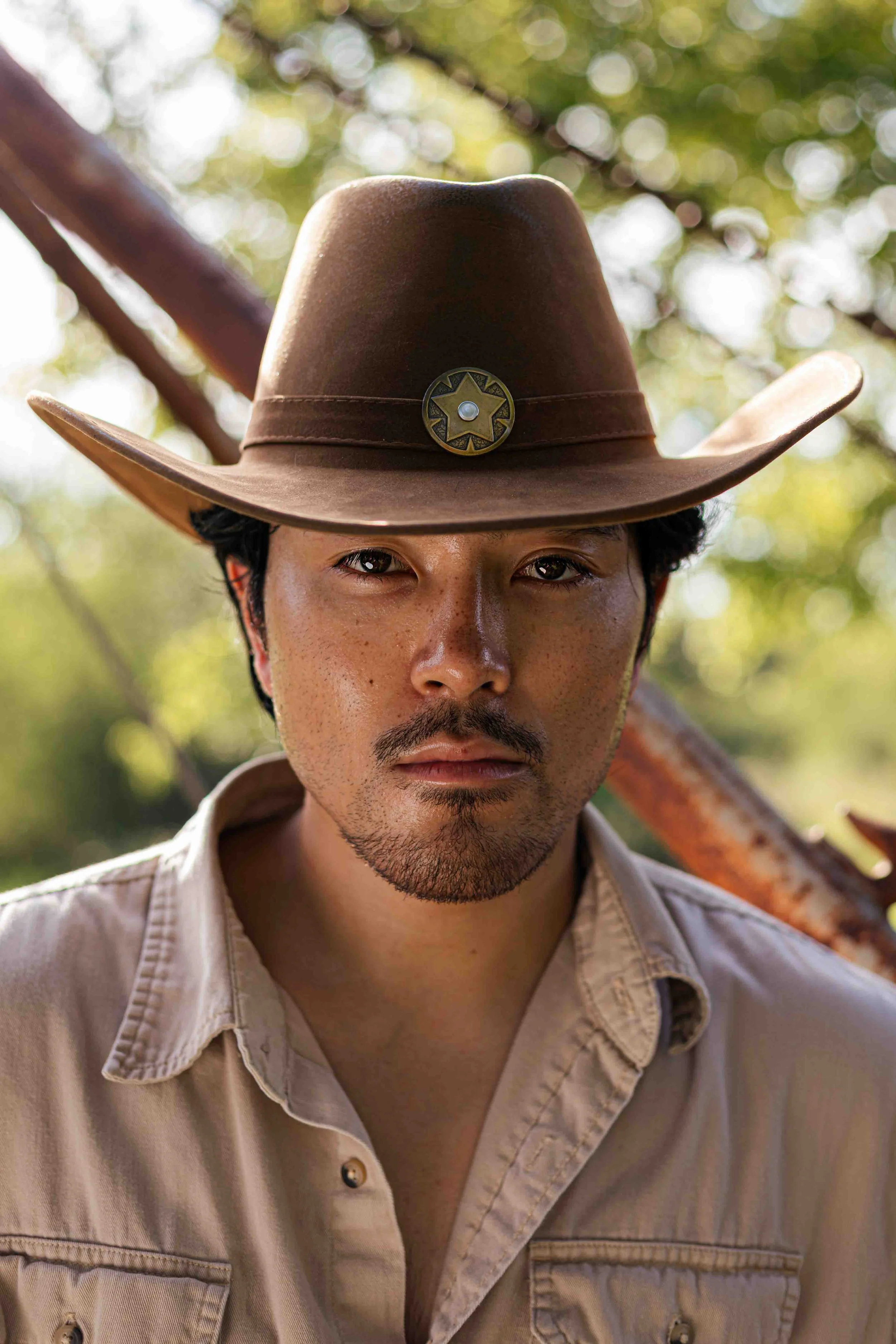 Houston editorial portrait close-up of a man wearing a cowboy hat with a star badge, outdoors with blurred trees in the background