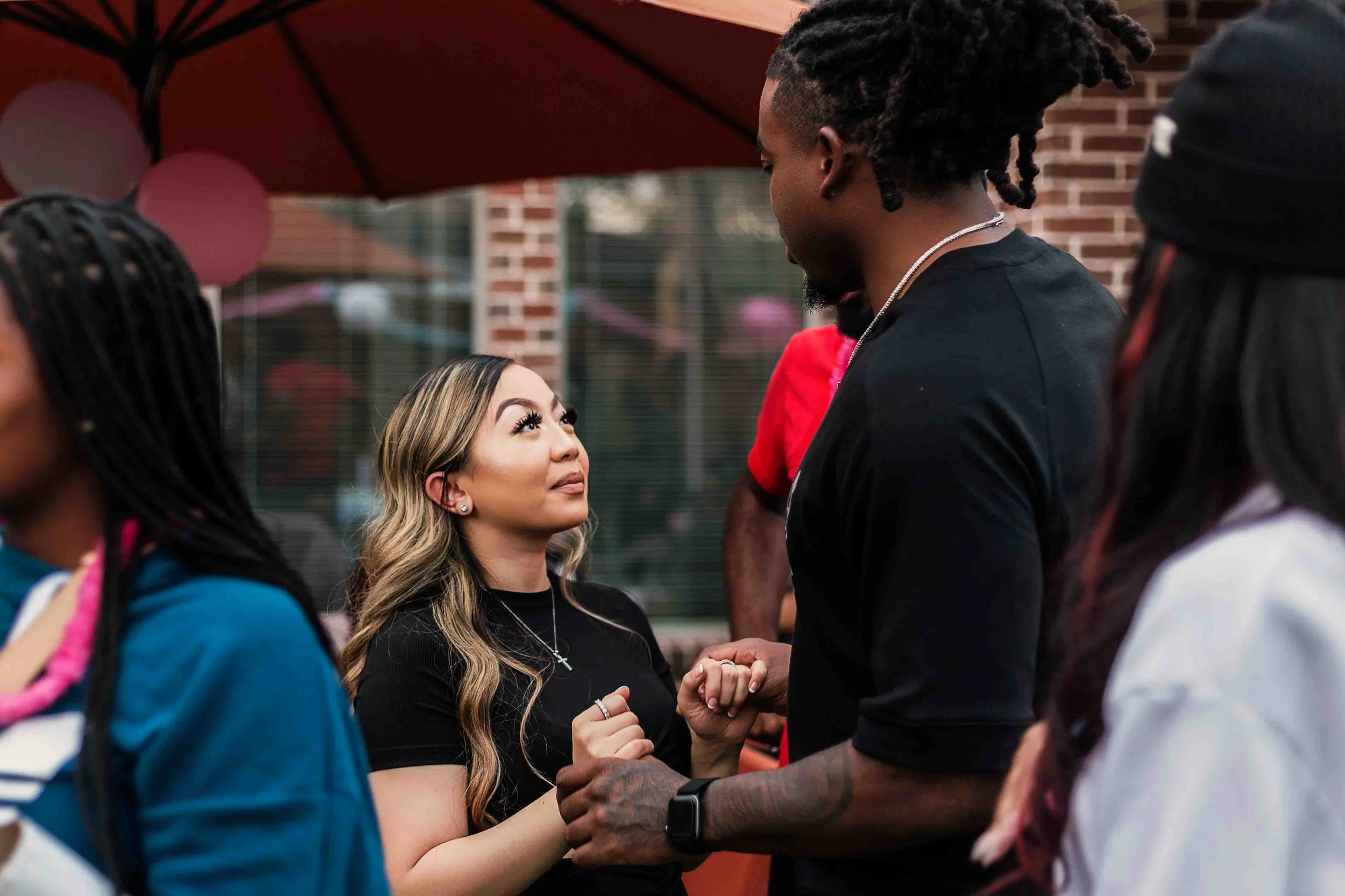 Outdoor couple portrait in Houston, Texas by Lev’s Photography featuring a woman and man holding hands and looking at each other during a gathering, with balloons and other people in the background