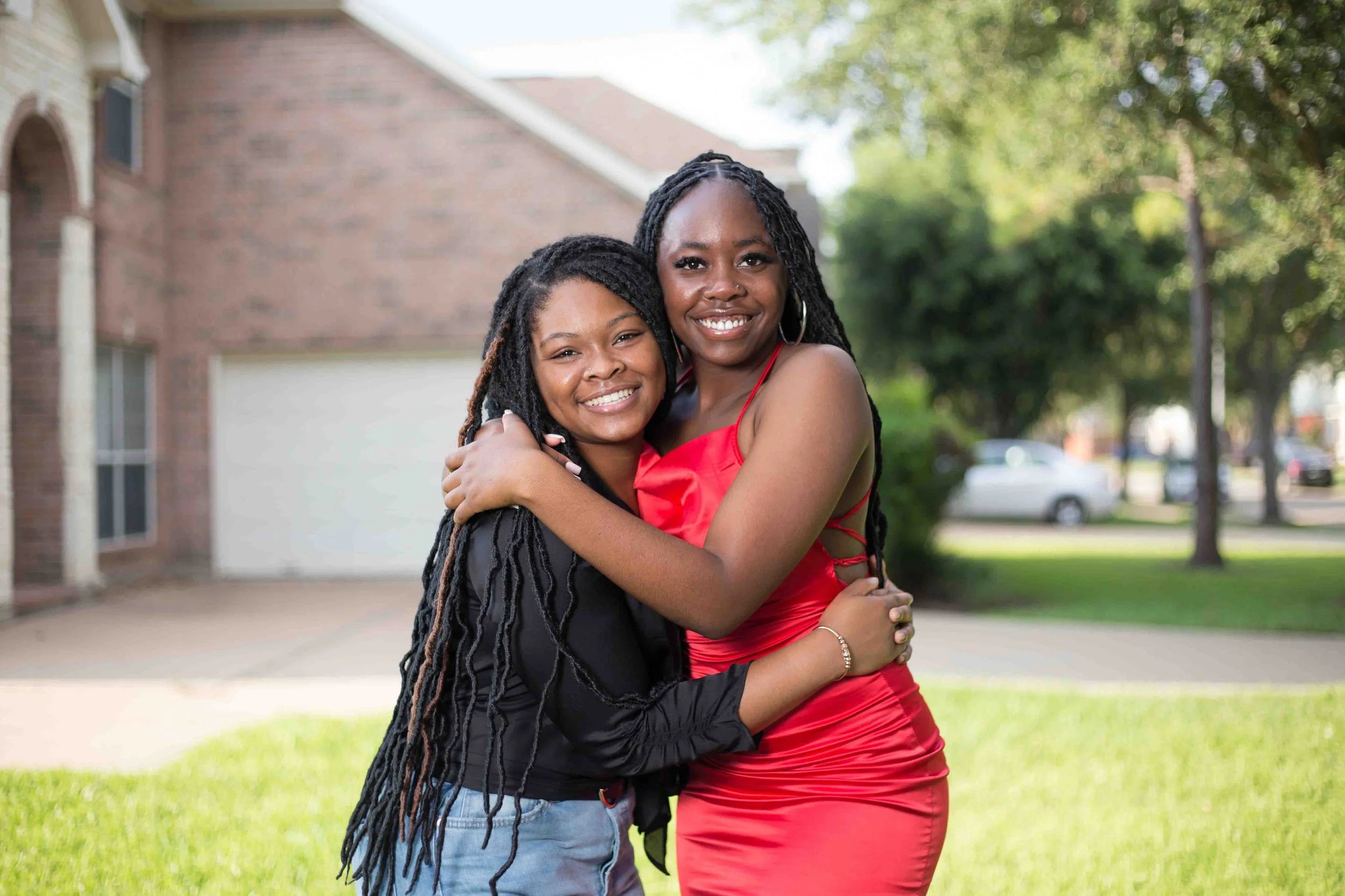 Birthday house event portrait in Houston, Texas by Lev’s Photography featuring two women hugging and smiling outdoors in front of a brick home and trees