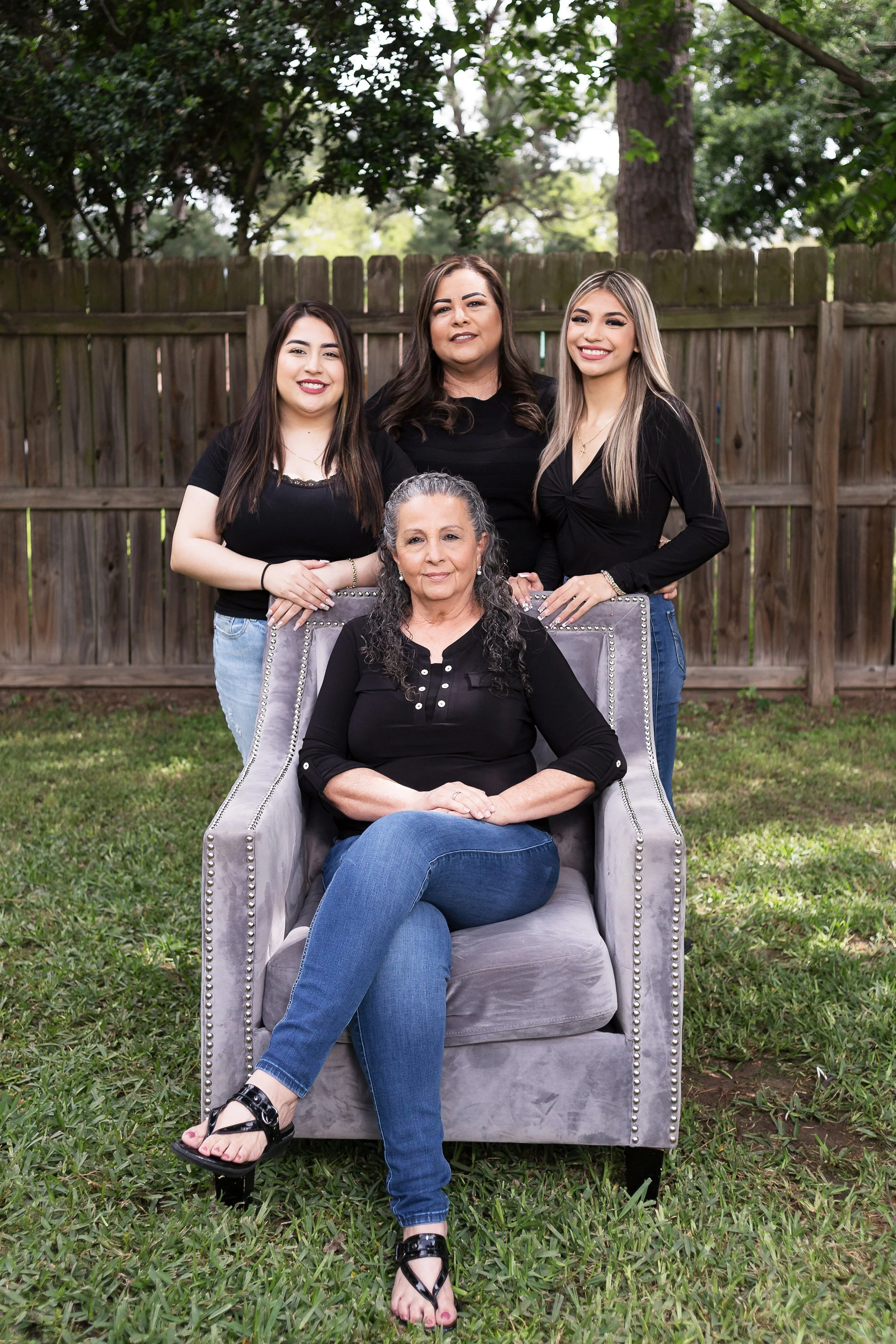 A woman sitting on a gray armchair outdoors with three young women standing behind her.