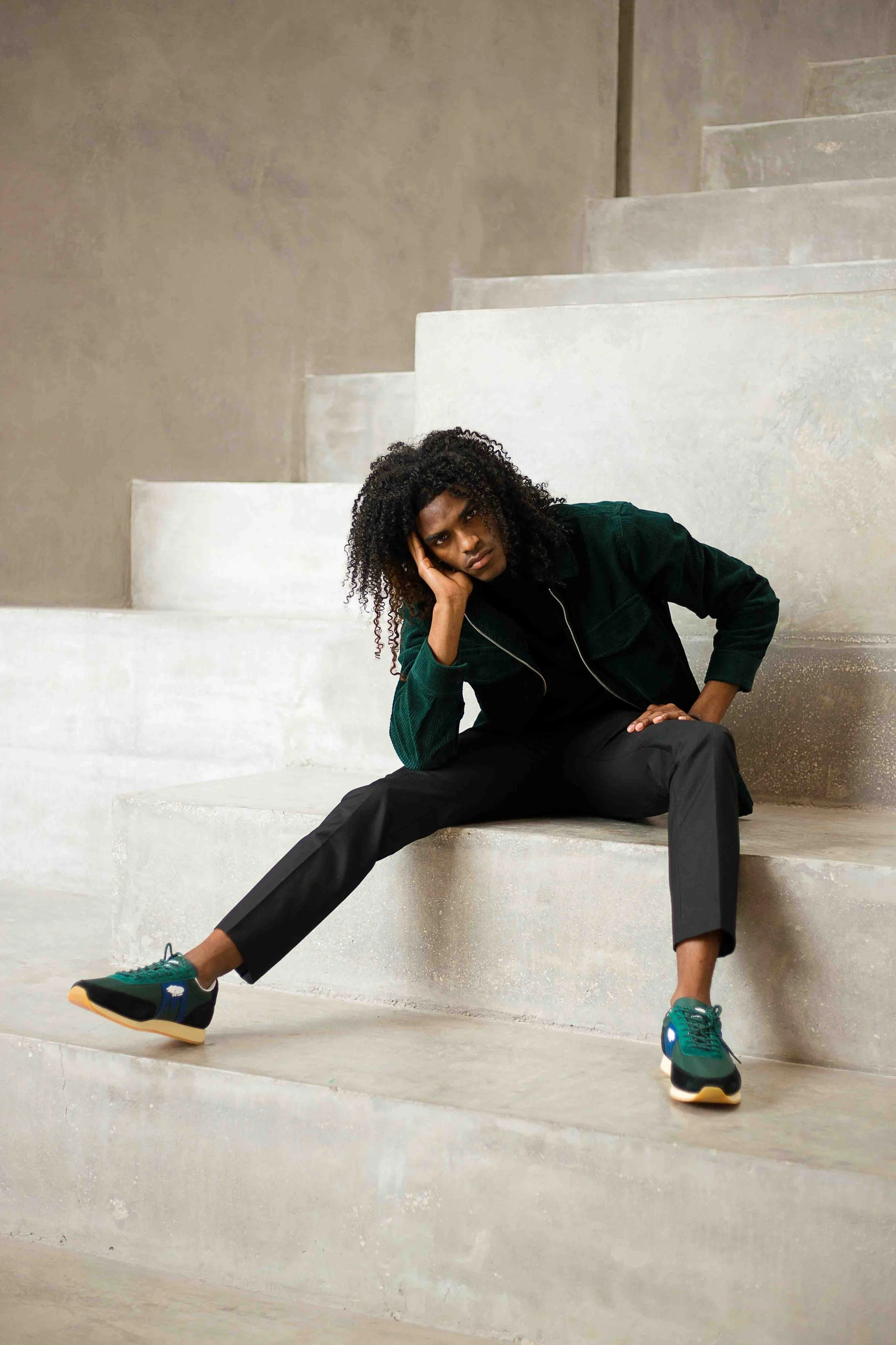 Urban portrait session in Houston, Texas by Lev’s Photography featuring a man in a dark green jacket and black pants posing on concrete stairs with a relaxed, editorial-style stance