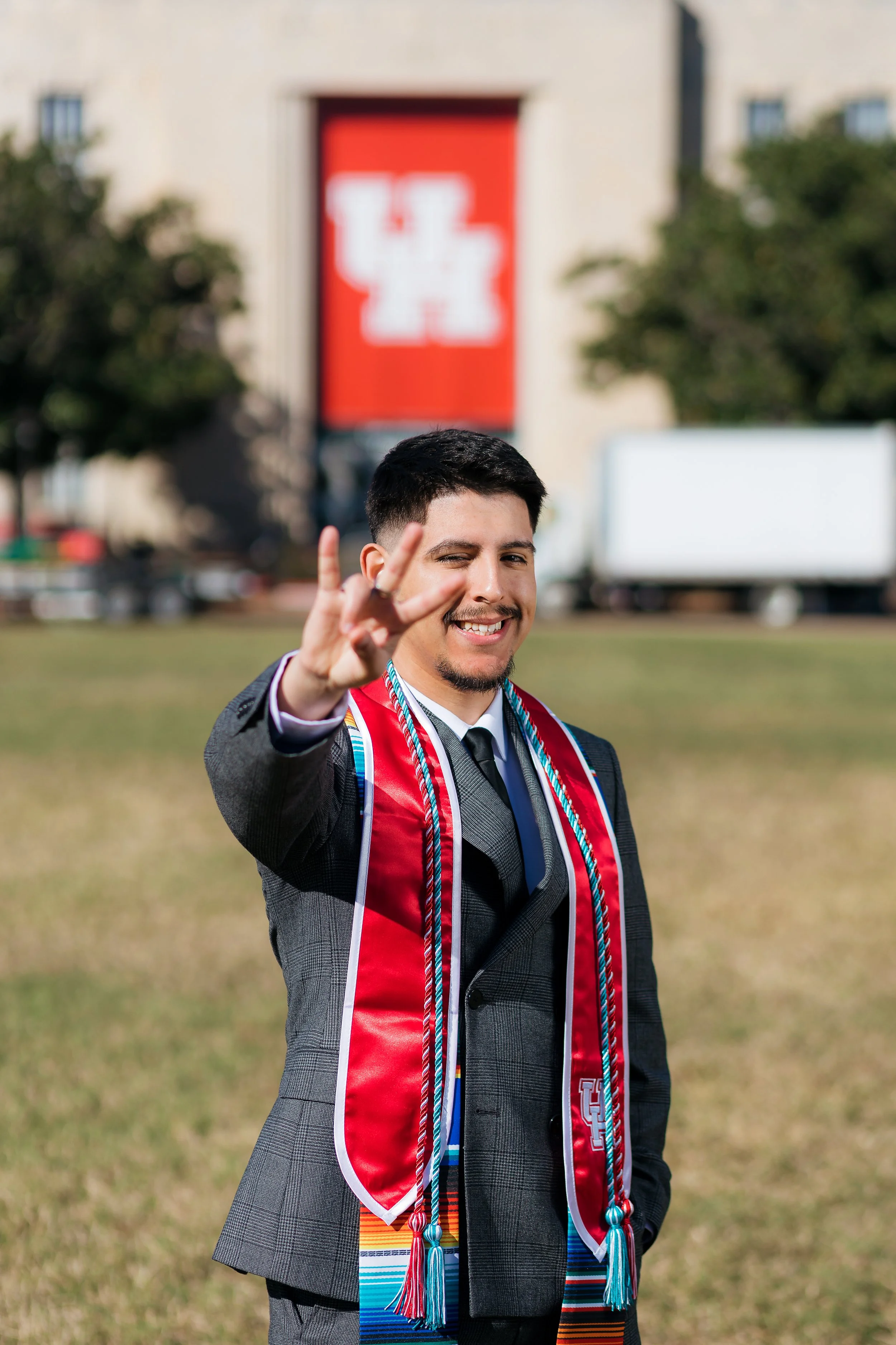 A young man in a suit with a graduation stole and honor cords making a peace sign at graduation.
