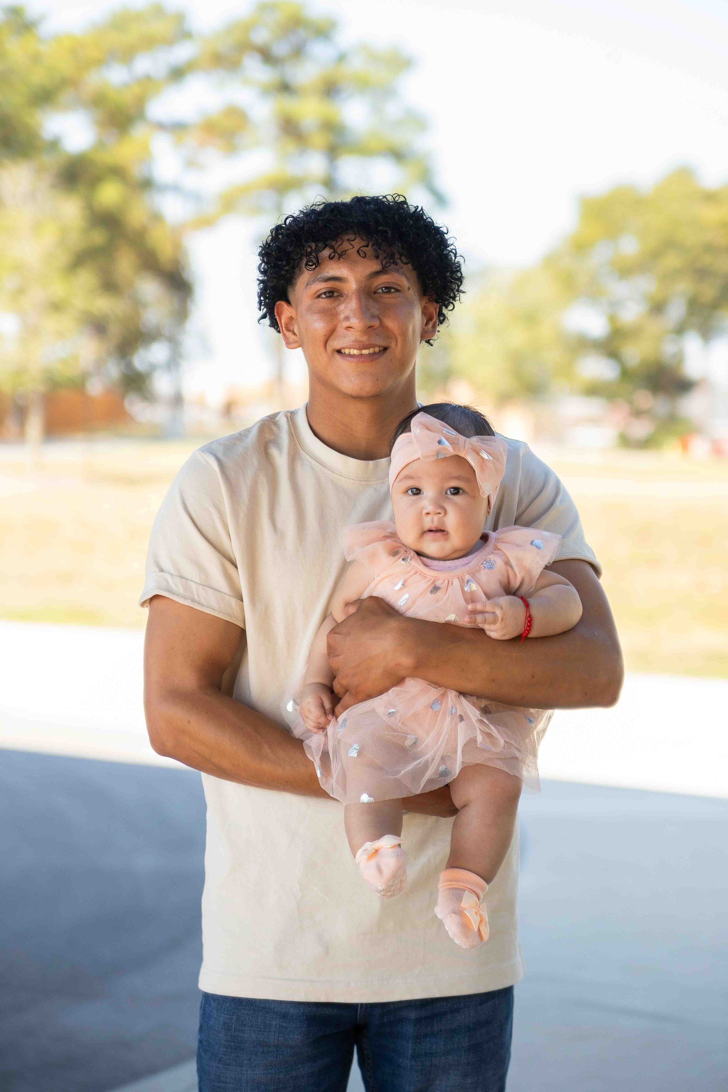 Outdoor family portrait in Houston, Texas by Lev’s Photography featuring a smiling man holding a young girl in a pink dress with a bow headband in a natural setting