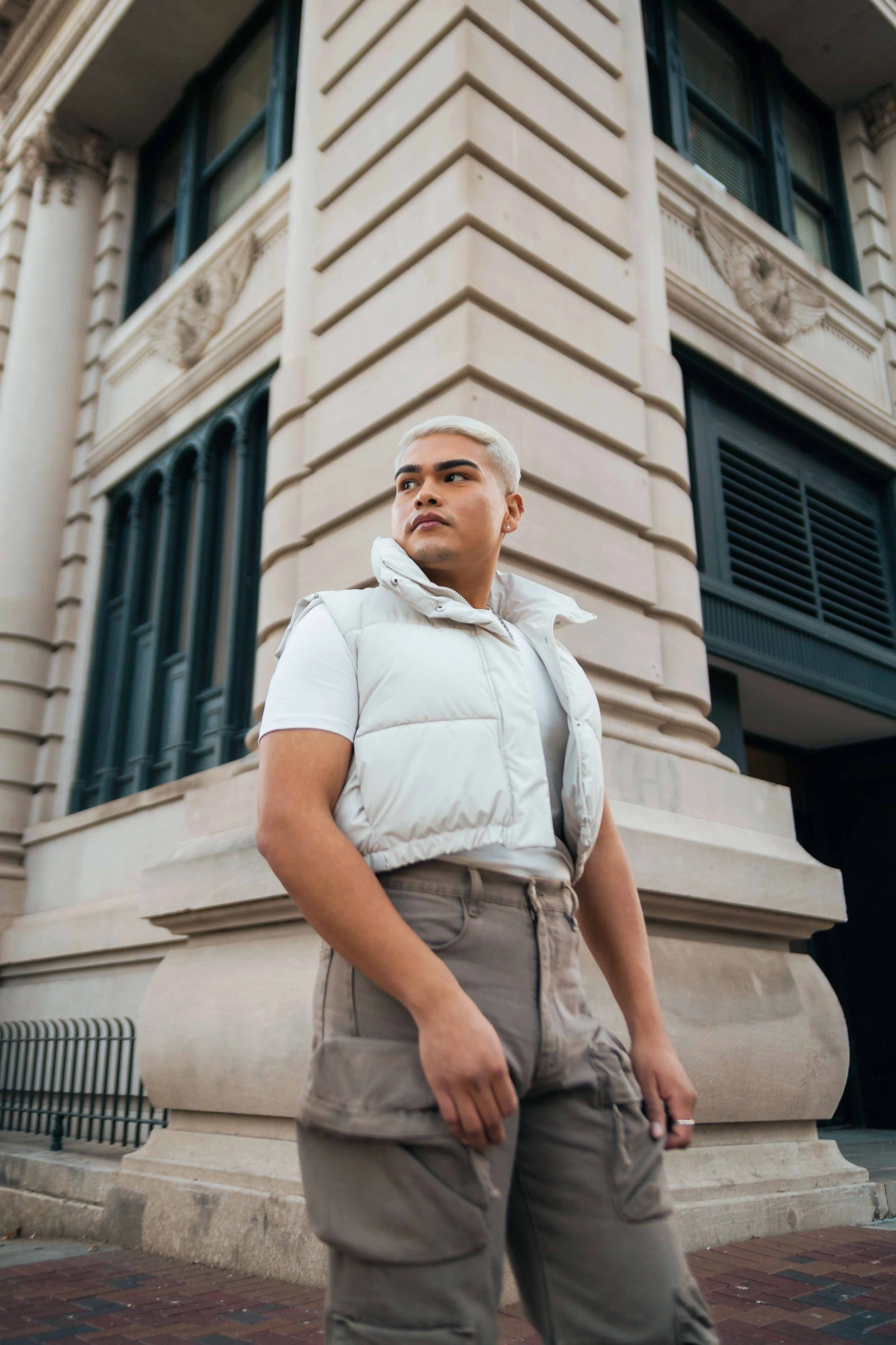 Birthday portrait session in downtown Houston, Texas by Lev’s Photography featuring a person wearing a white vest and beige cargo pants standing in front of a historic building with ornate architectural details.