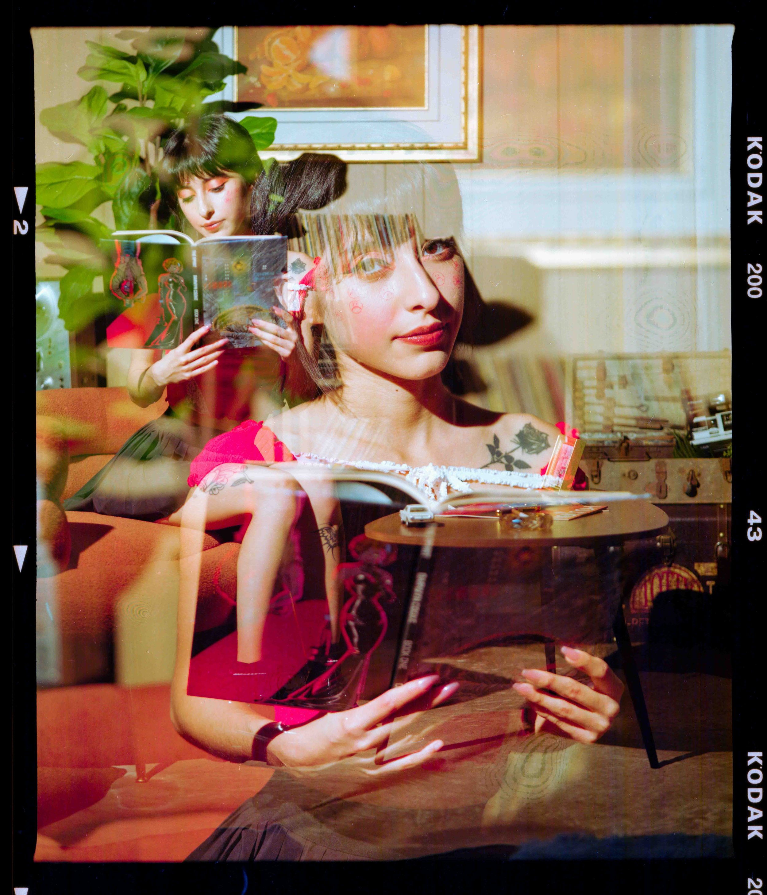 Cinematic editorial portrait on 120 film featuring multiple exposures of a tattooed woman reading on a couch, professionally lit with framed artwork and bookshelves in the background