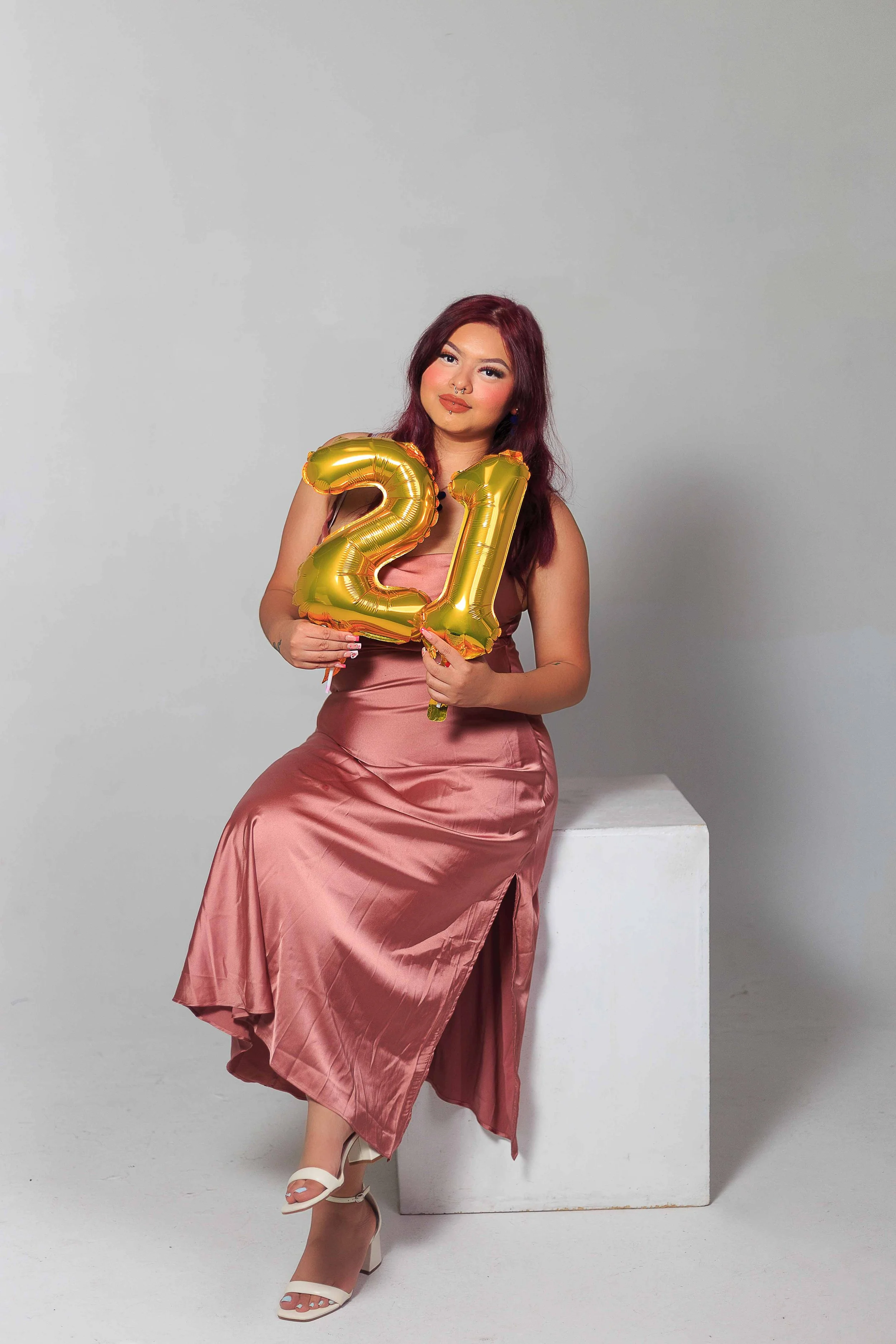 21st birthday studio portrait in Houston, Texas by Lev’s Photography featuring a woman in a pink satin dress holding gold “21” balloons against a light background