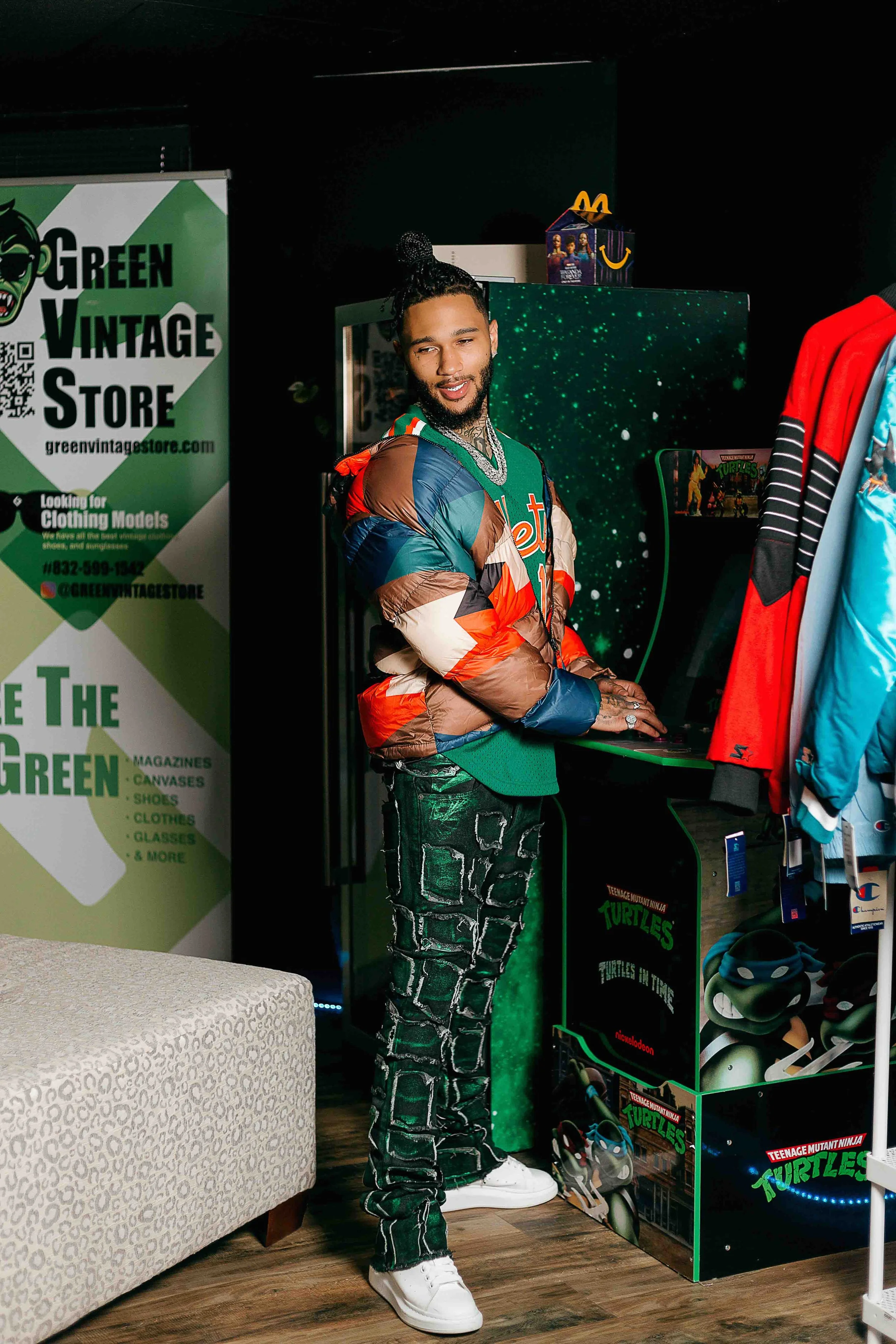 Creative lifestyle portrait in Houston, Texas by Lev’s Photography featuring a young man with braids and tattoos wearing a colorful puffer jacket while using an arcade machine beside Teenage Mutant Ninja Turtles merchandise