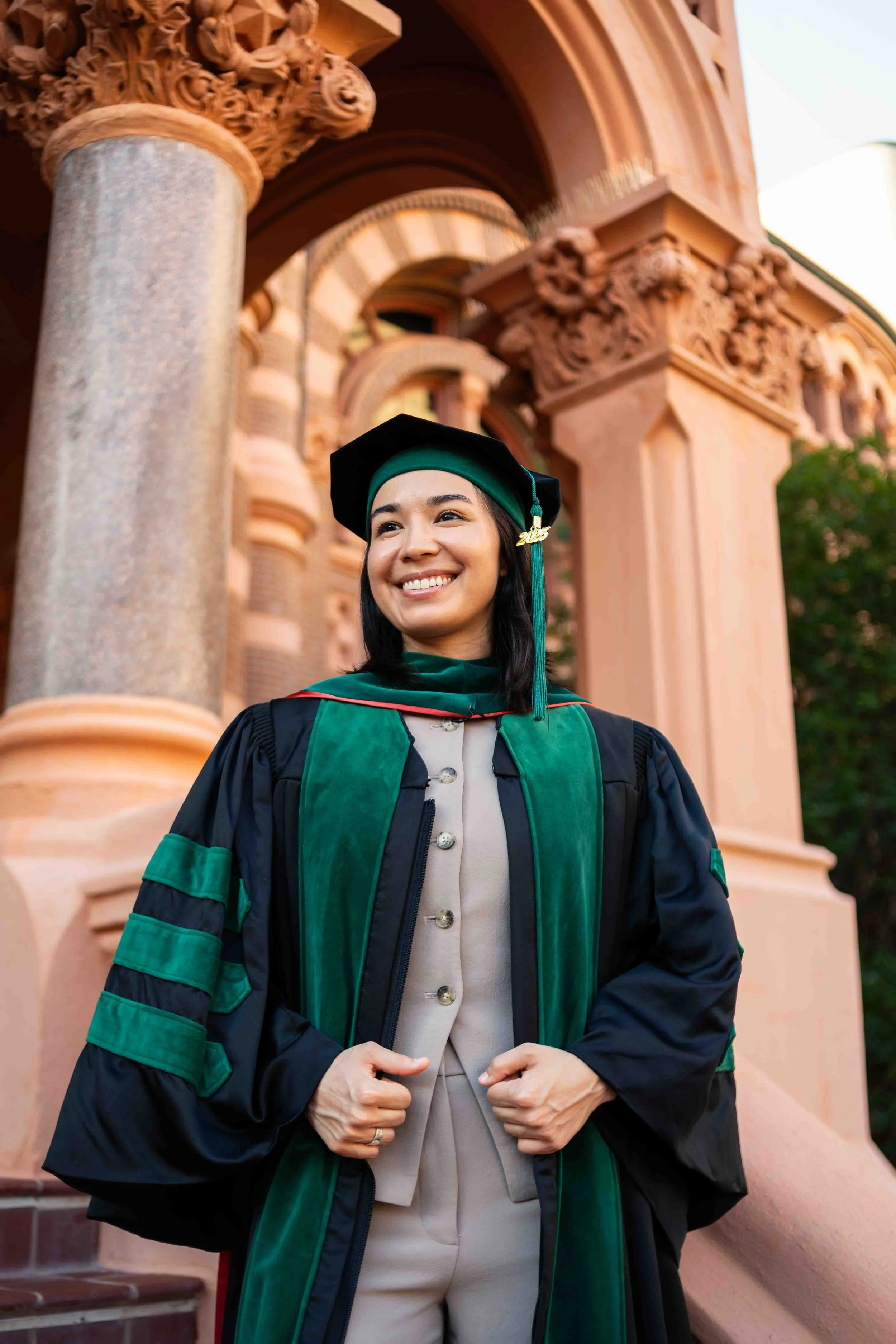 Senior graduation photo of a young woman in cap and gown posing in front of the historic Old Red building in Galveston, showcasing its ornate pink stone architecture