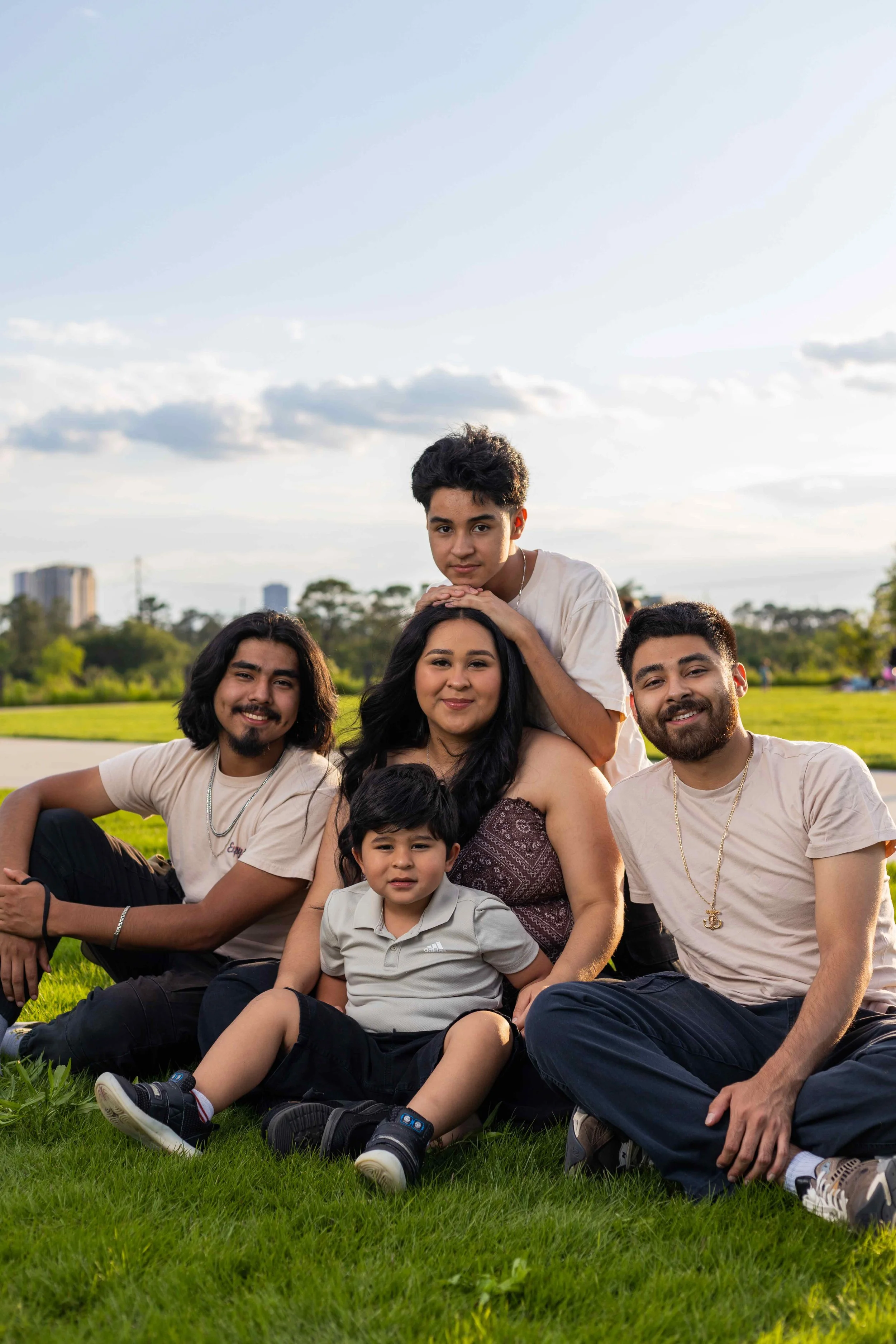 Family and sibling portrait session at Memorial Park in Houston, Texas by Lev’s Photography featuring a group sitting on the grass with trees and the city skyline in the background