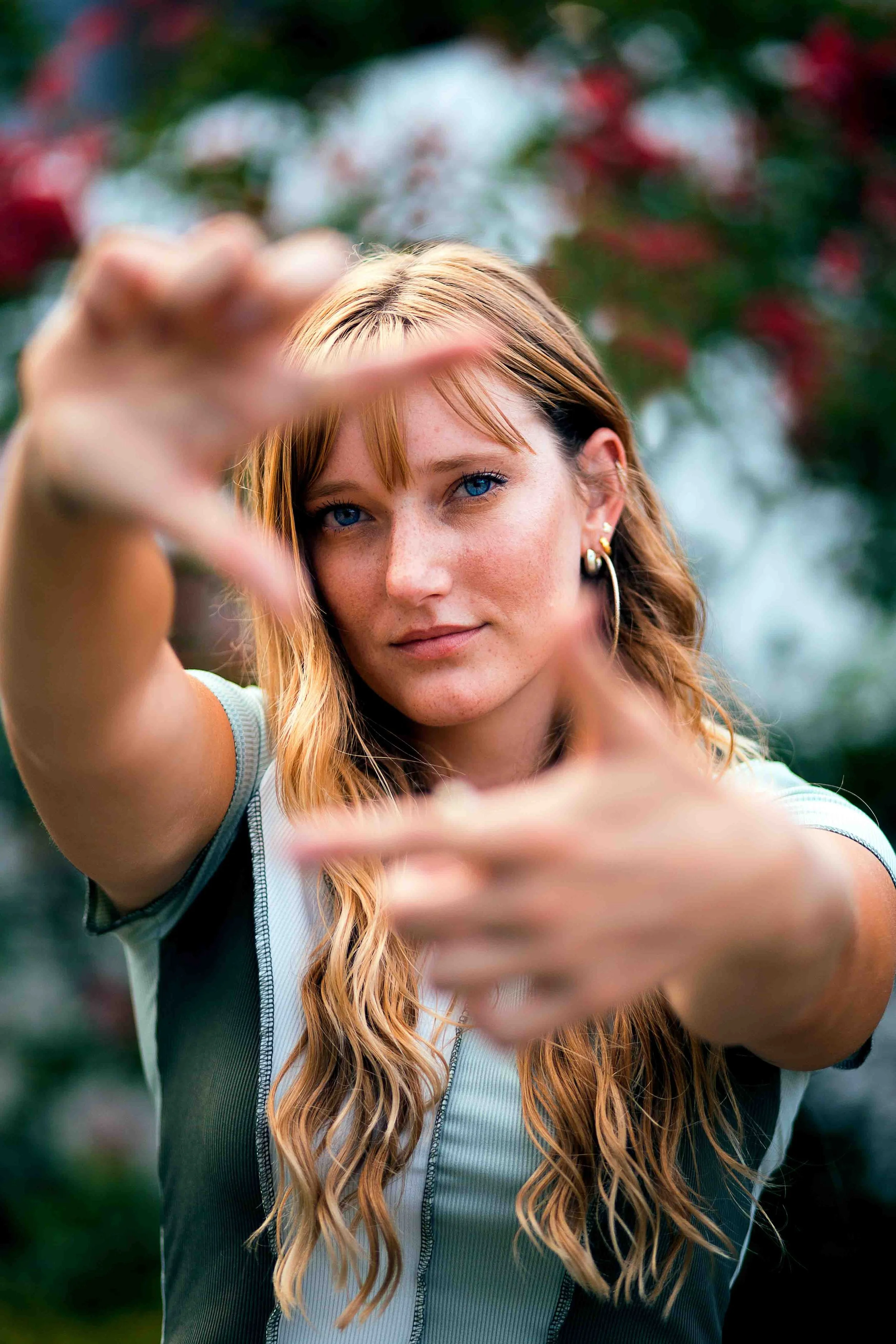 Downtown portrait by Levs Photography in Houston, Texas featuring a young woman with red hair and blue eyes forming a heart shape with her hands, captured outdoors with soft natural light and an urban city backdrop.