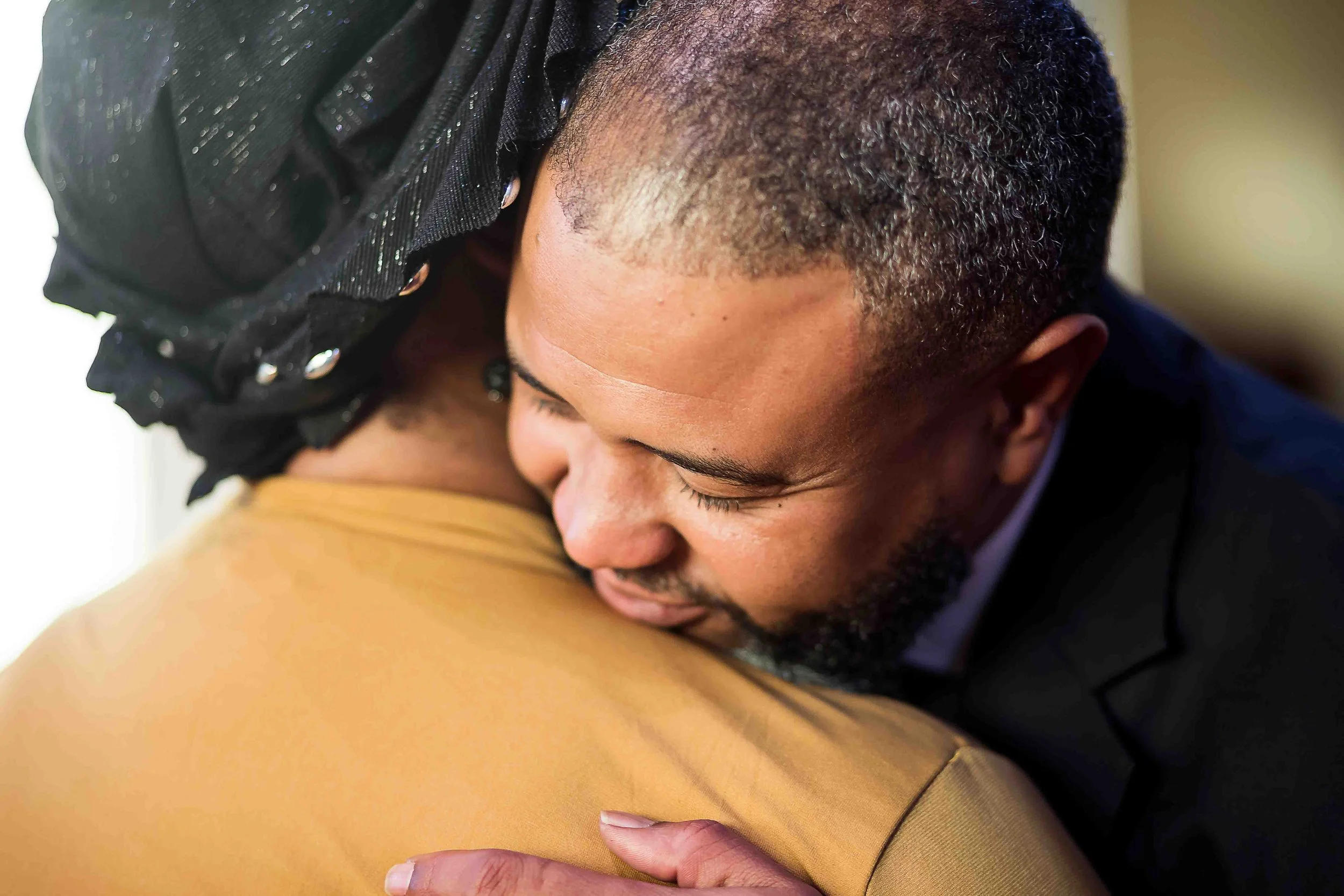 Houston church service portrait by Lev's Photography capturing an emotional moment between a man in a suit and a woman wearing a black embellished headscarf and mustard top, embracing with heads resting together during Sunday worship, highlighting co