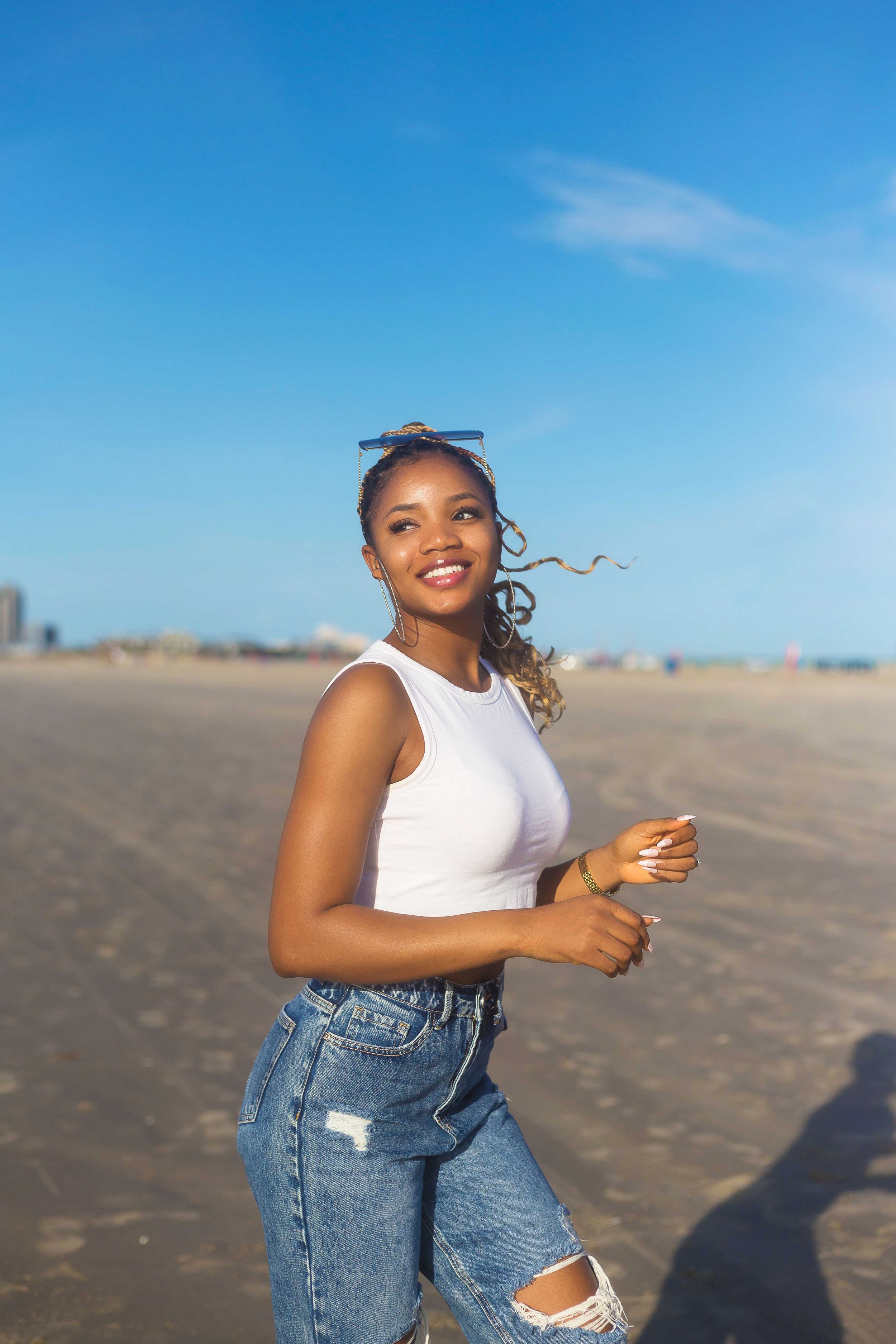 Woman smiling and looking left during an engagement photoshoot at Galveston Beach with sunny shoreline and distant buildings in the background