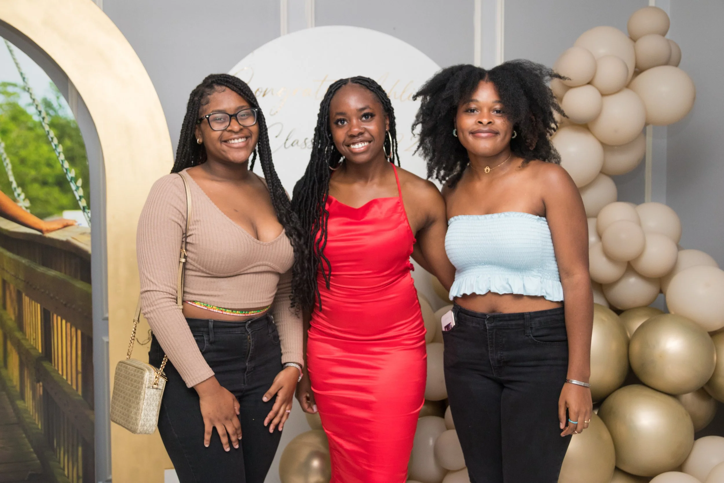 Three women standing together at a celebration, with balloons in the background, smiling at the camera.