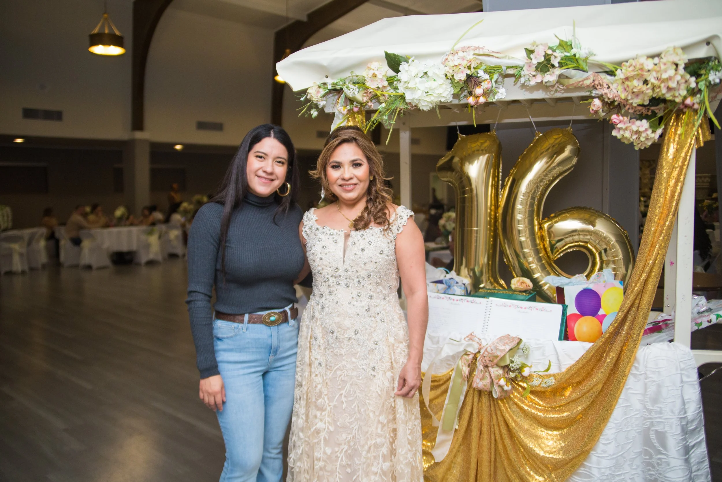 Two women standing together at a 16th birthday party decorated with gold balloons and floral arrangements.