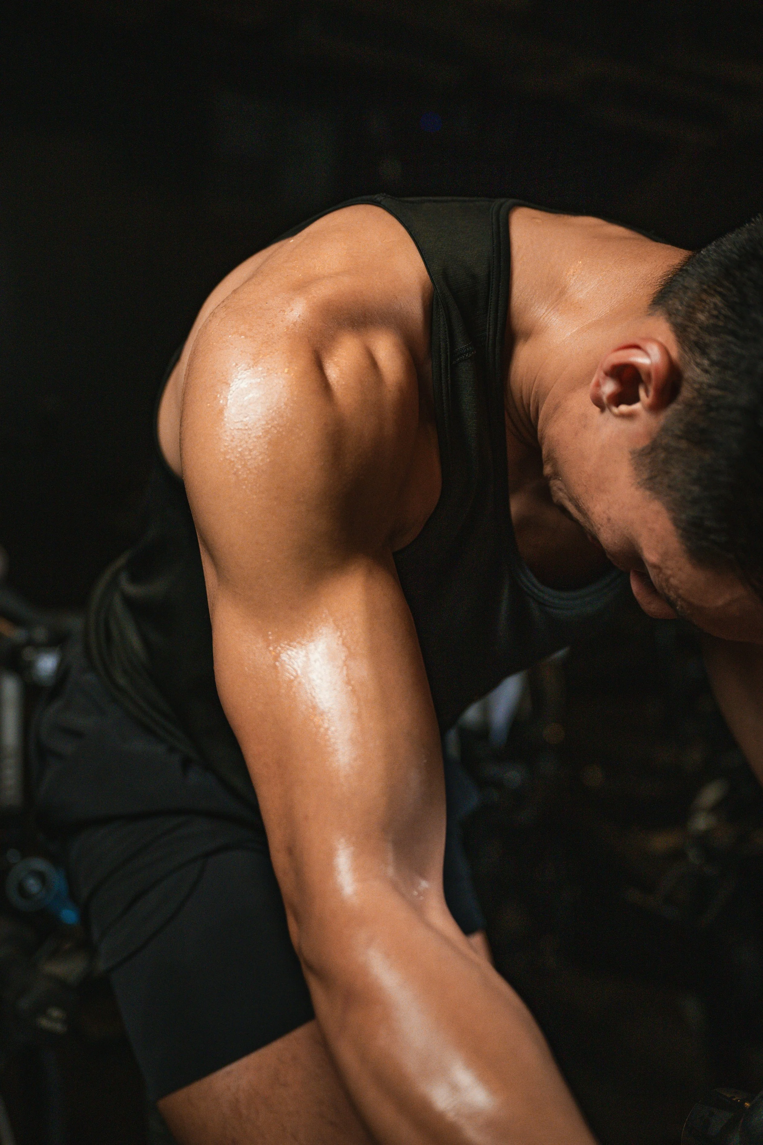 A person in black workout attire is sweating, bent forward, with their head down, focusing on exercise.