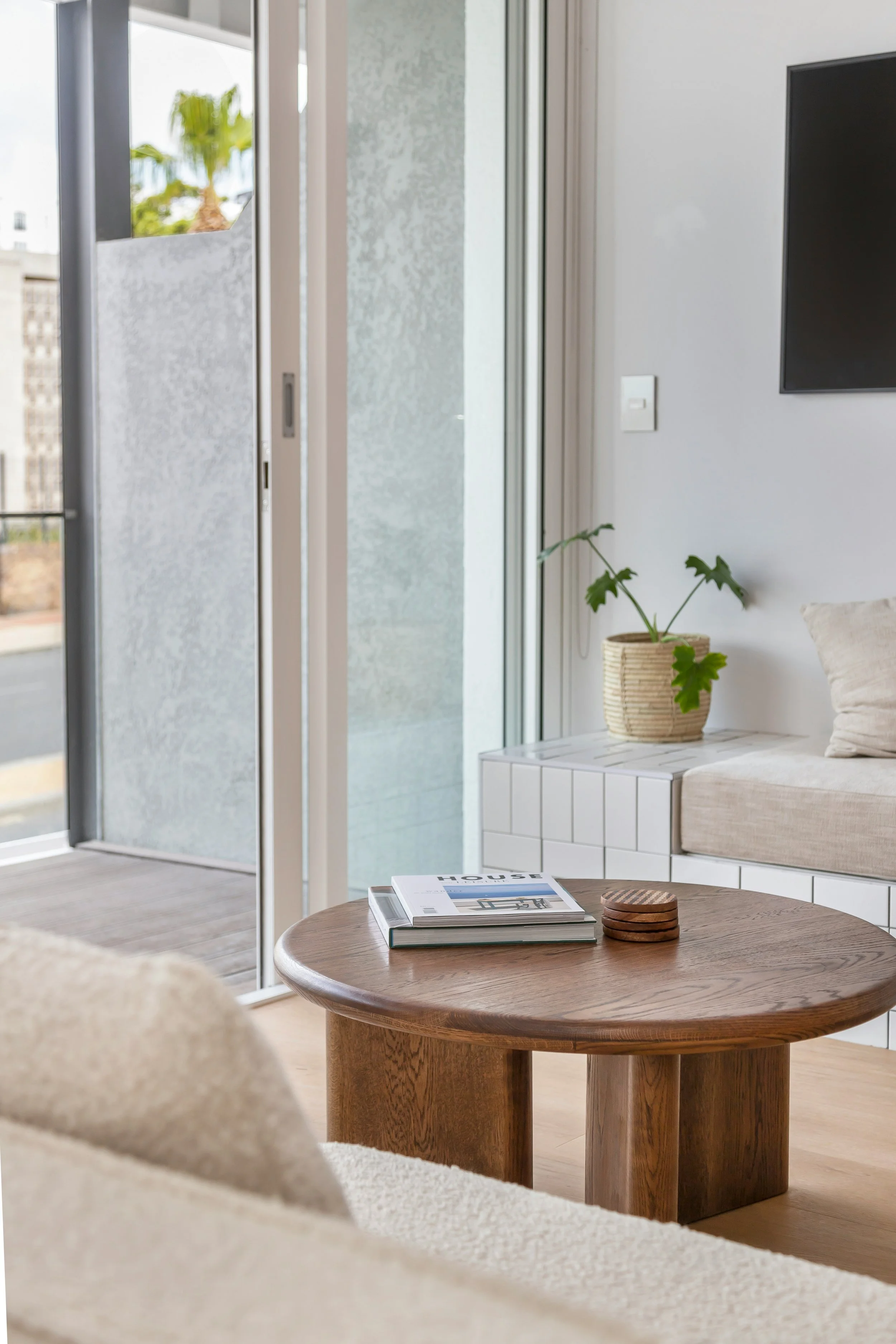 Elegant minimalist living room featuring white couches arranged around a round wooden coffee table, accentuated by simple decor and natural light.