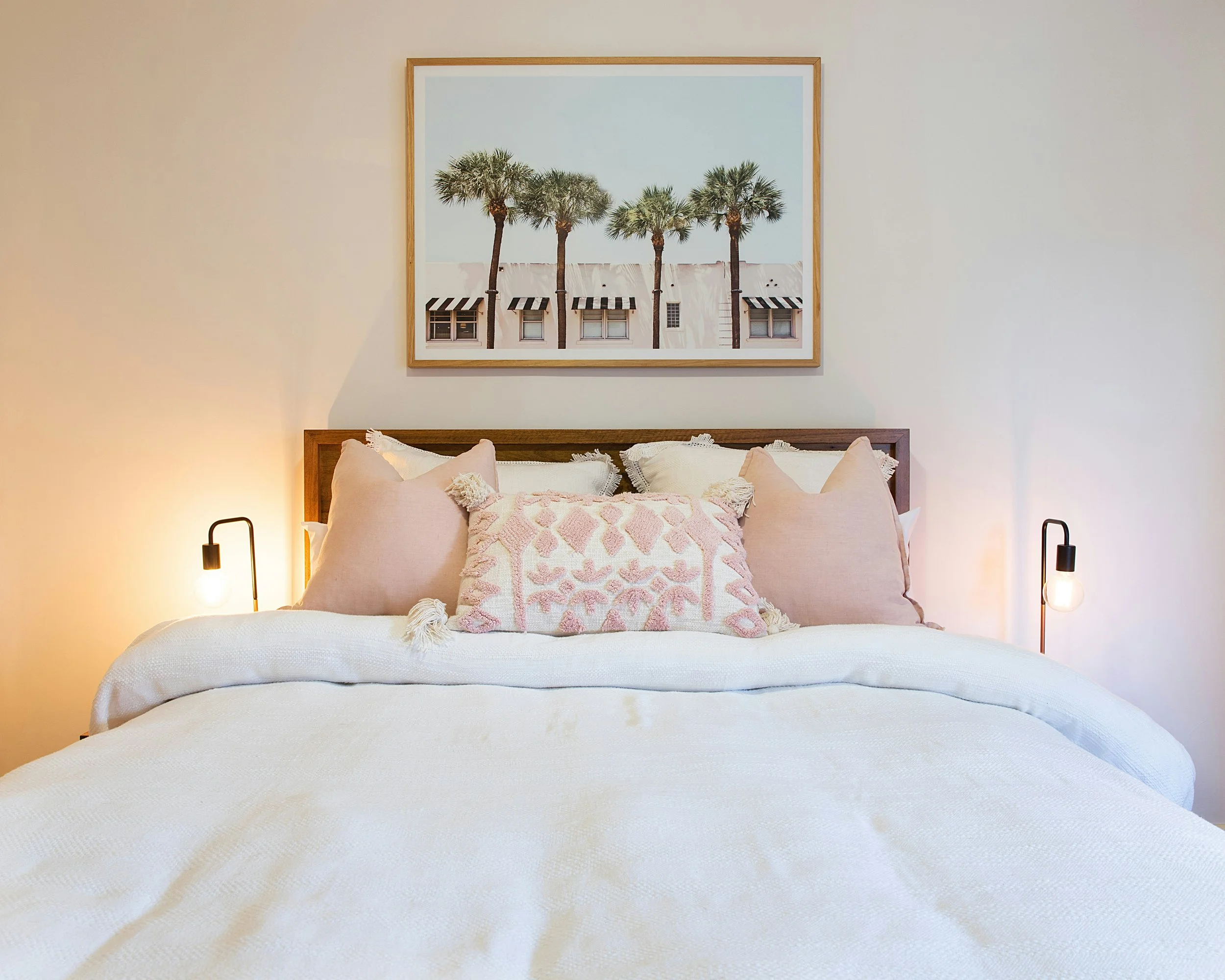 Cozy bedroom featuring a plush bed adorned with decorative throw pillows and a vibrant palm tree image on the wall, creating a tropical and inviting retreat.