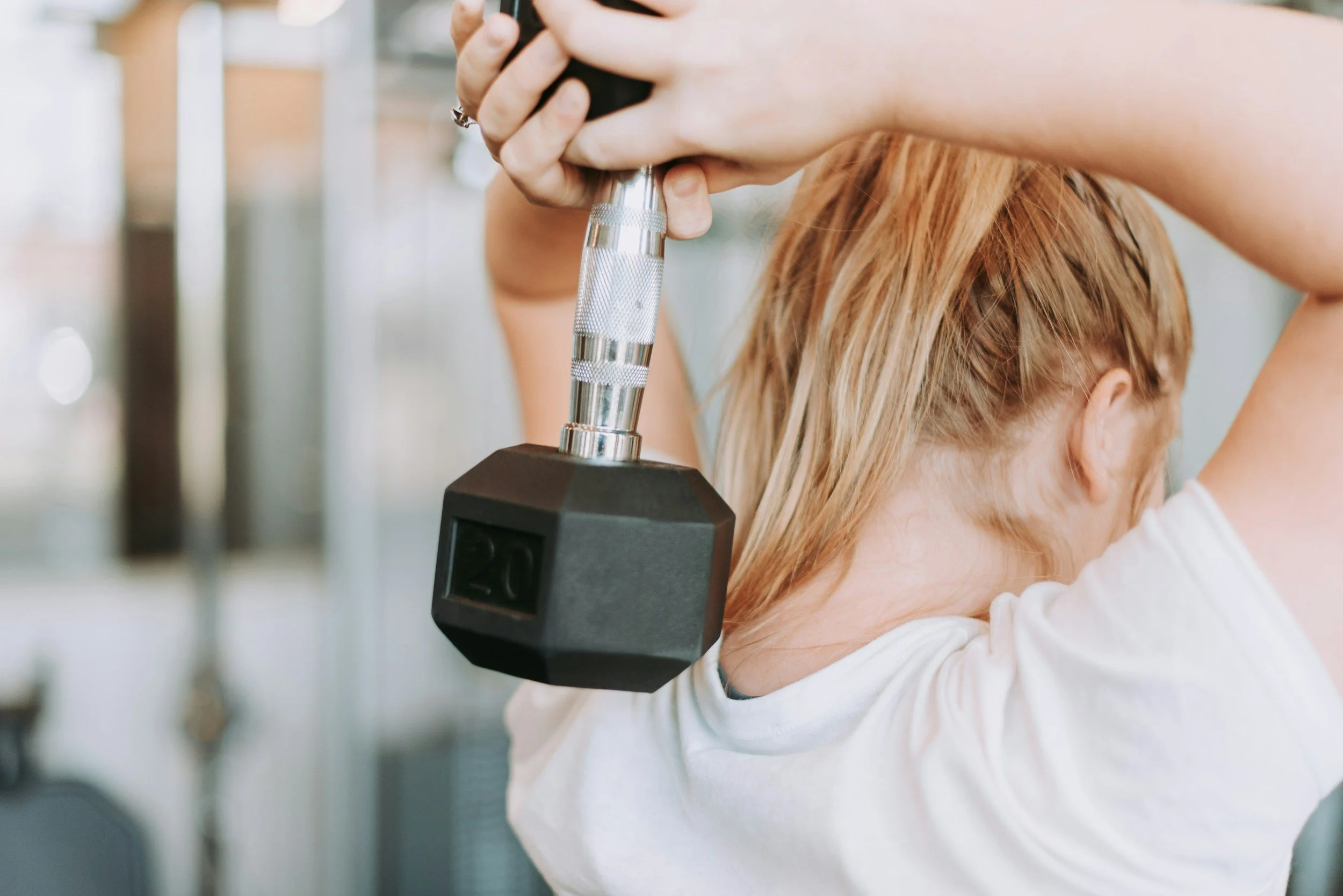 A woman lifting a dumbbell onto her neck at the gym.