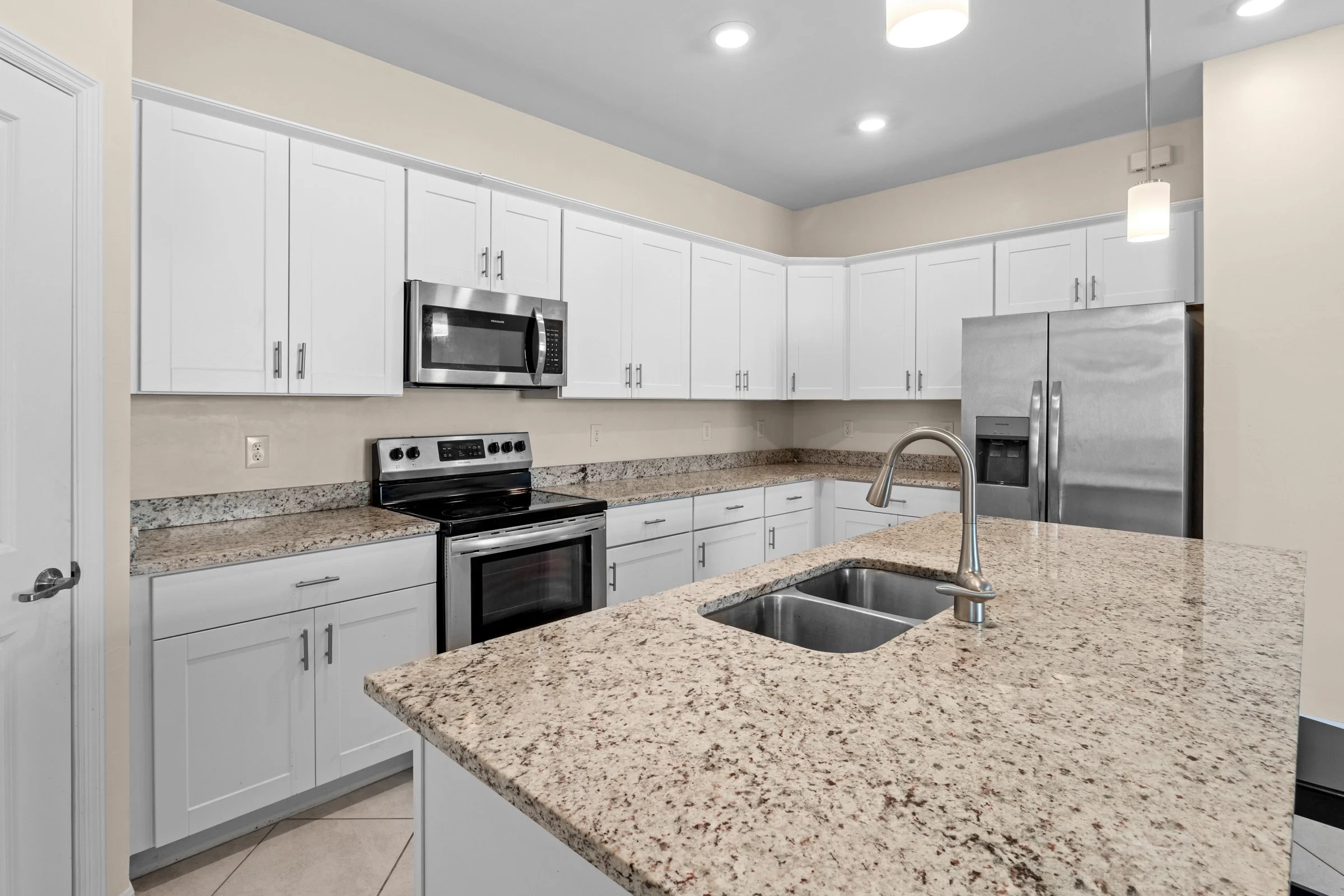 Modern kitchen with white cabinets, granite countertops, stainless steel appliances, and double sink