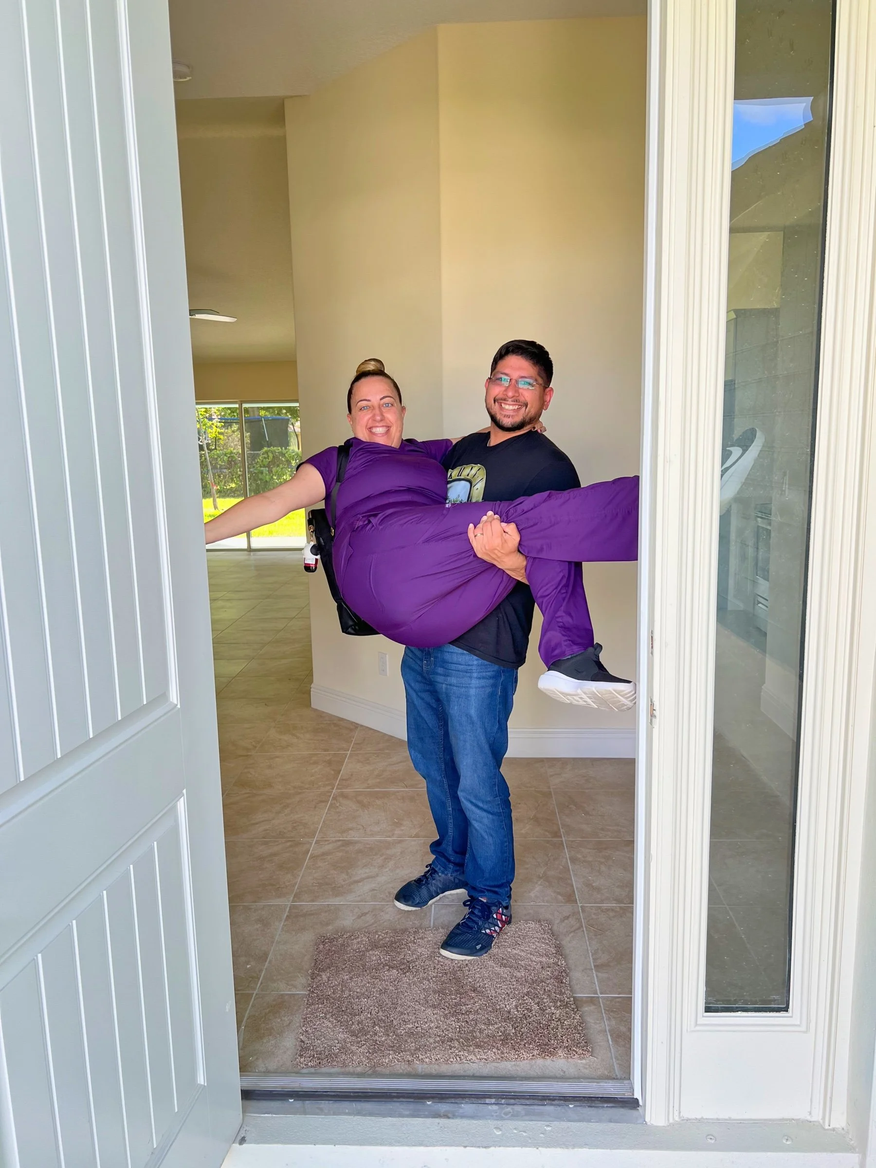 Man carrying a woman in purple into a house, doorway open, interior visible.