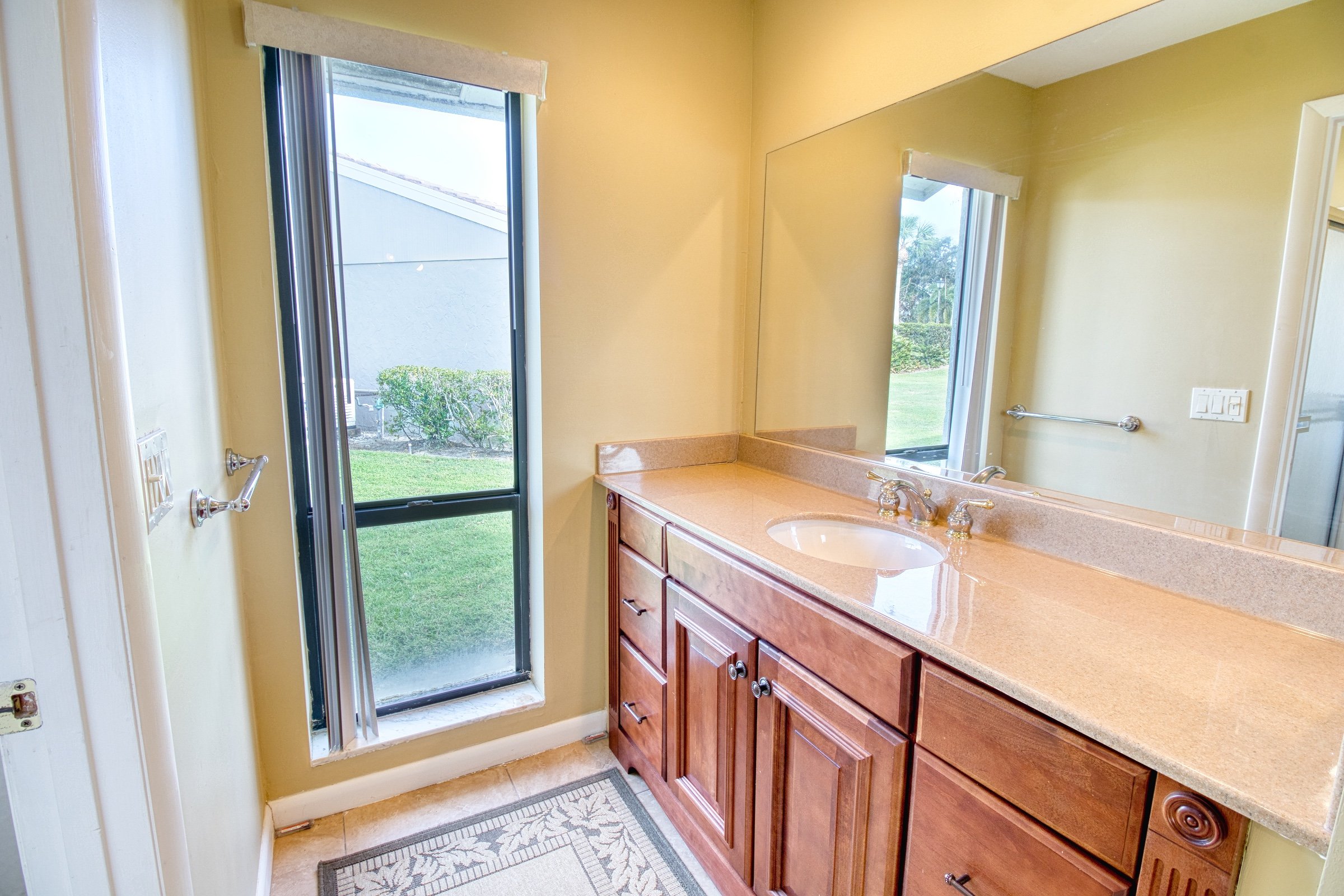 Modern bathroom with wooden cabinet, sink, large mirror, window, and beige walls.